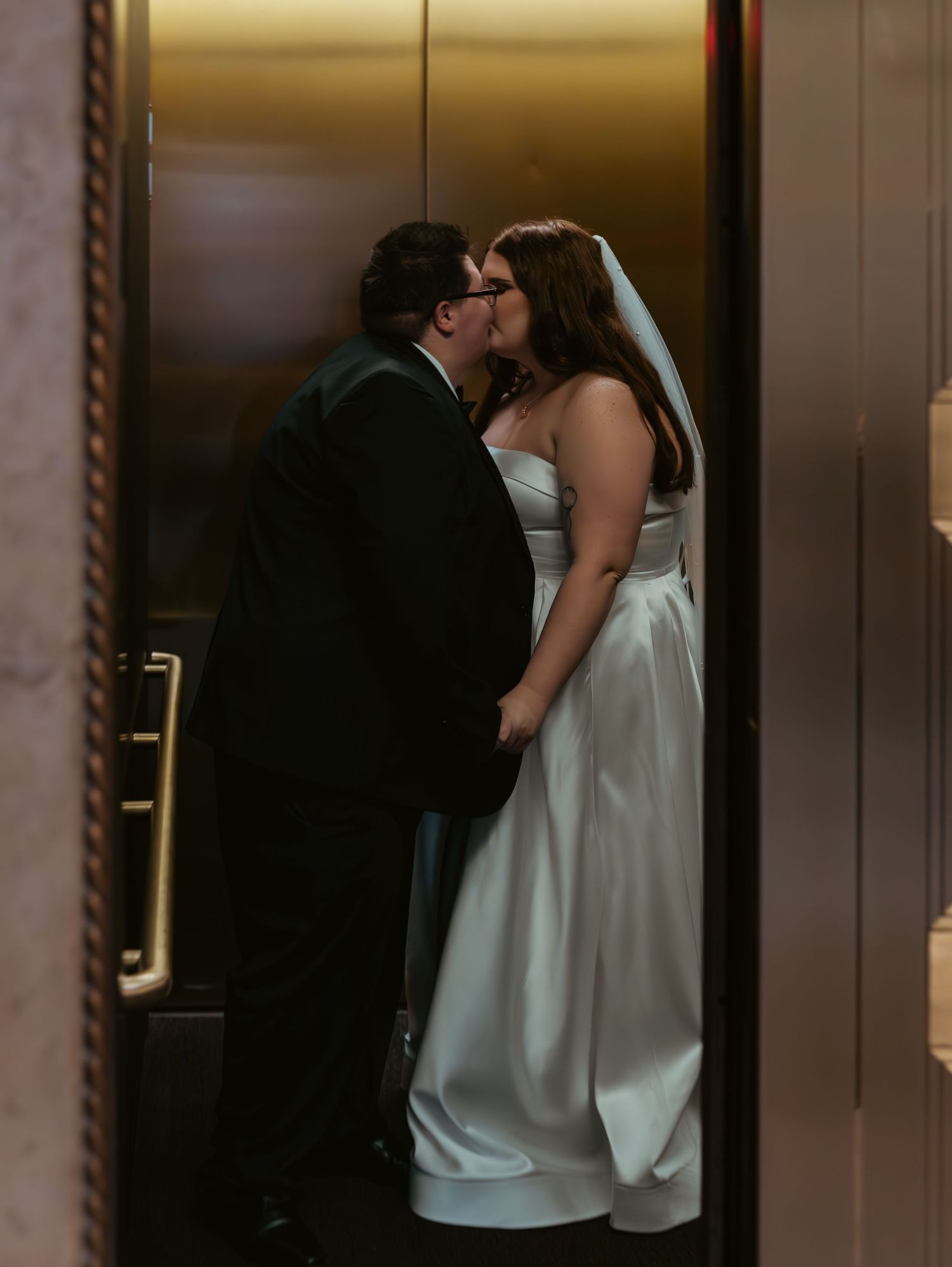 Couple in wedding attire sharing an intimate moment near a brown wooden door.