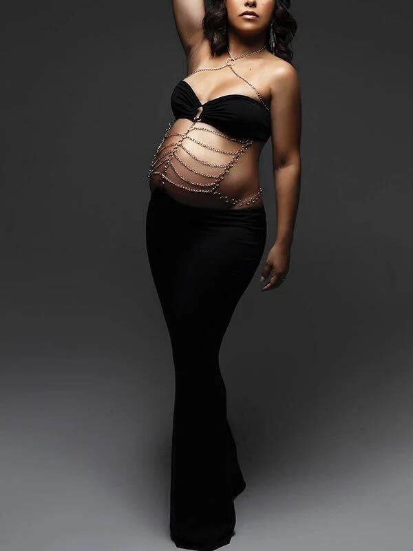 Dramatic fashion photo of model in black evening gown with chain body jewelry against dark background.