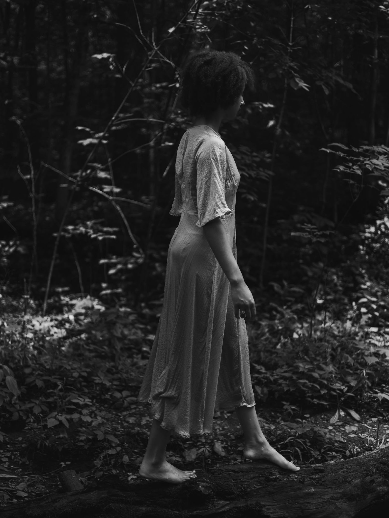 A black and white sequence of photos showing a person in a flowing dress walking through a dark forest setting.