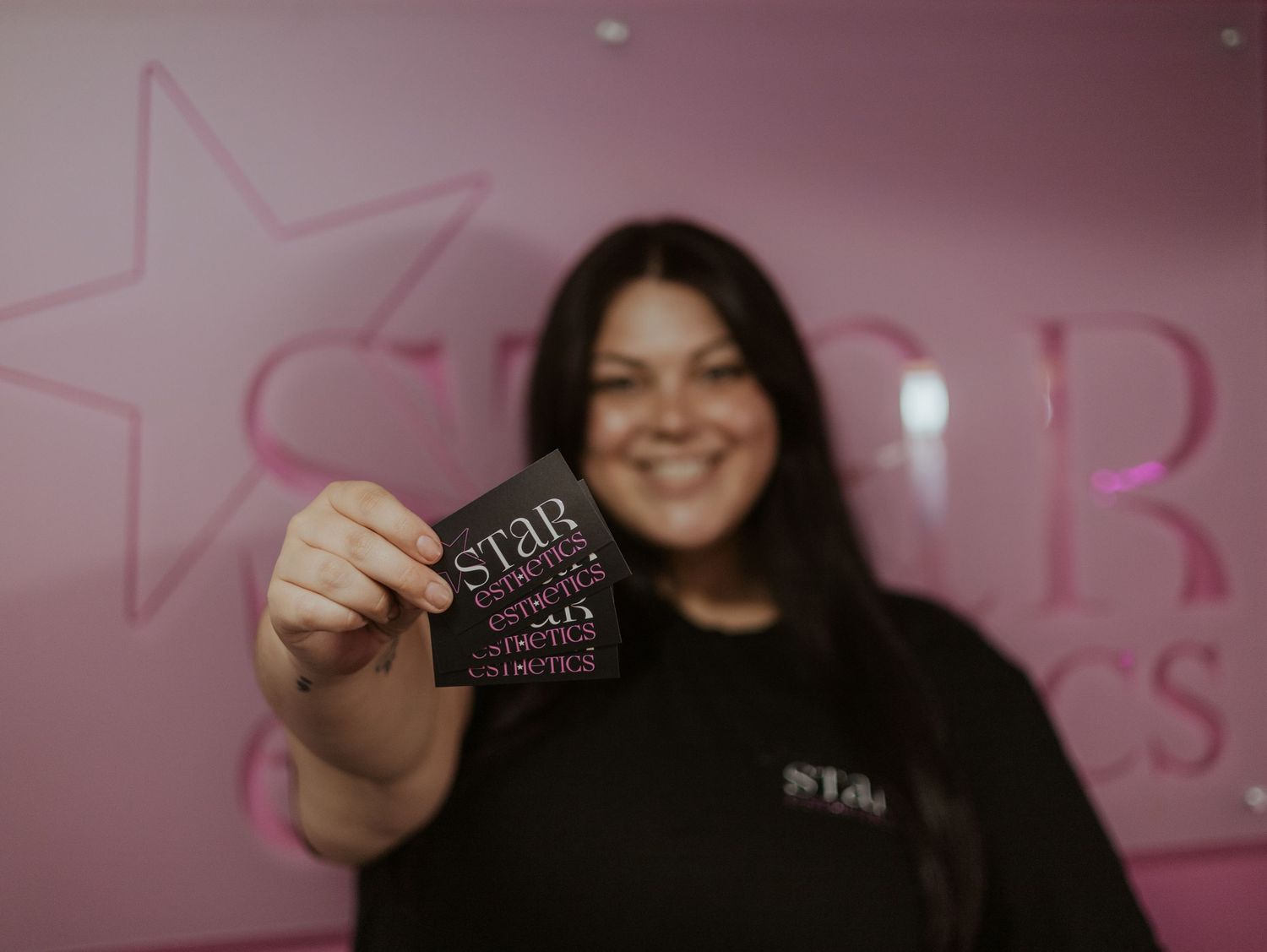 Someone holding up a Star membership card while smiling in front of a pink background with star decorations.