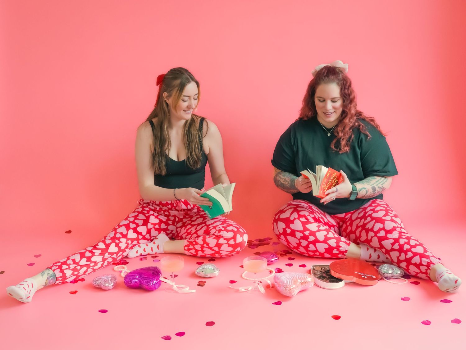 Friends in matching heart-print pajamas read books surrounded by Valentine's decorations.
