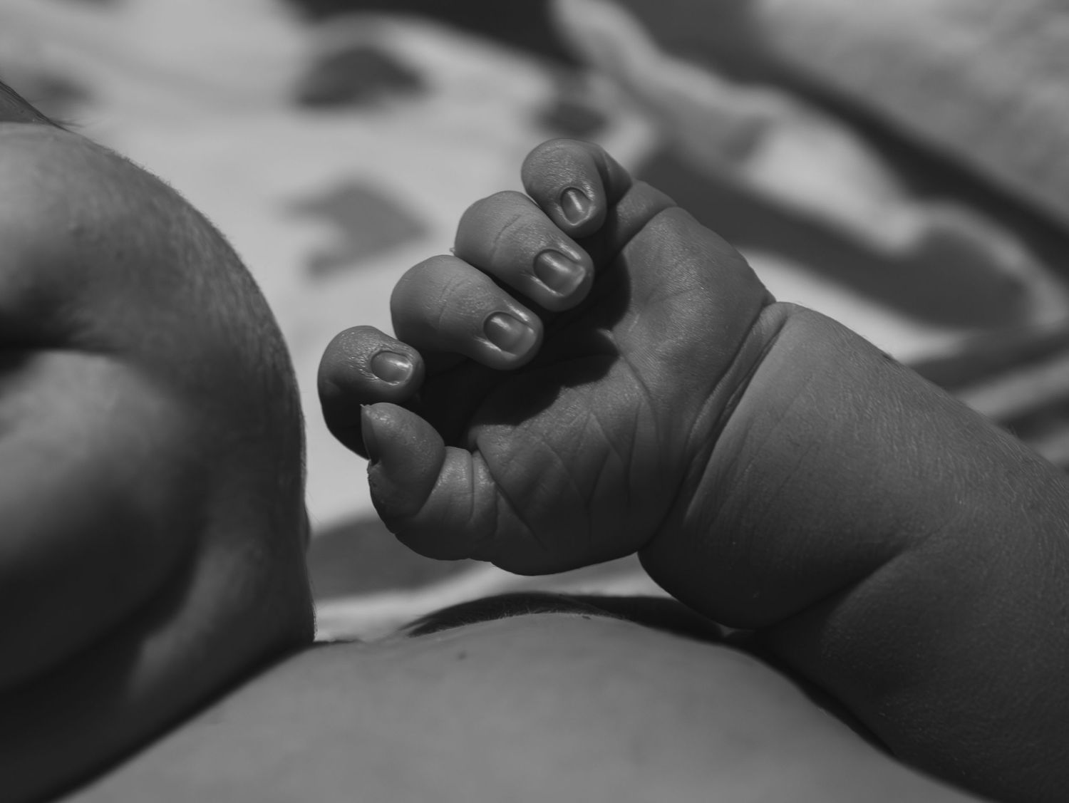 A tender black and white close-up shot of a tiny baby's fist against soft bedding.