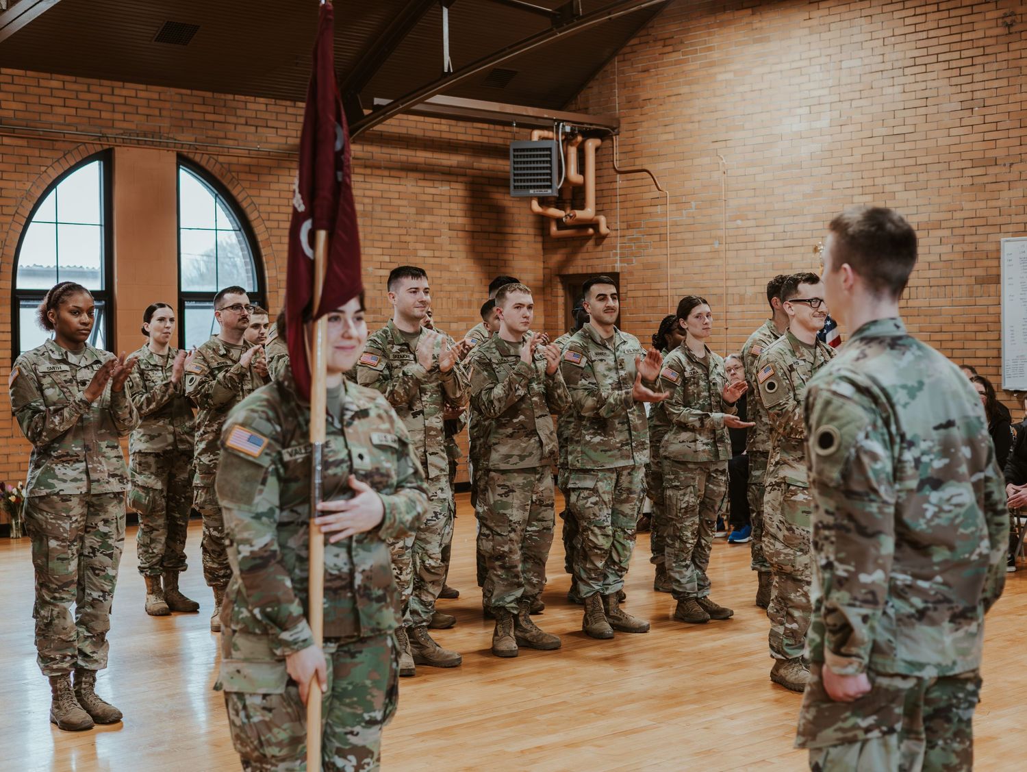 Military personnel in camouflage uniforms stand in formation inside a brick-walled room during a training exercise.