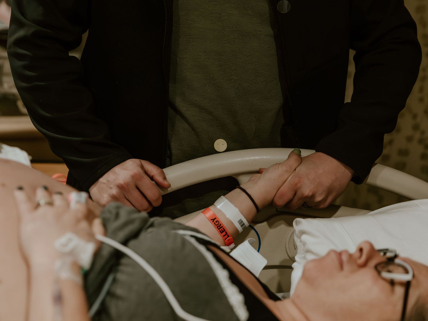 A patient receiving medical care in a hospital bed as a caregiver tends to them with medical equipment.