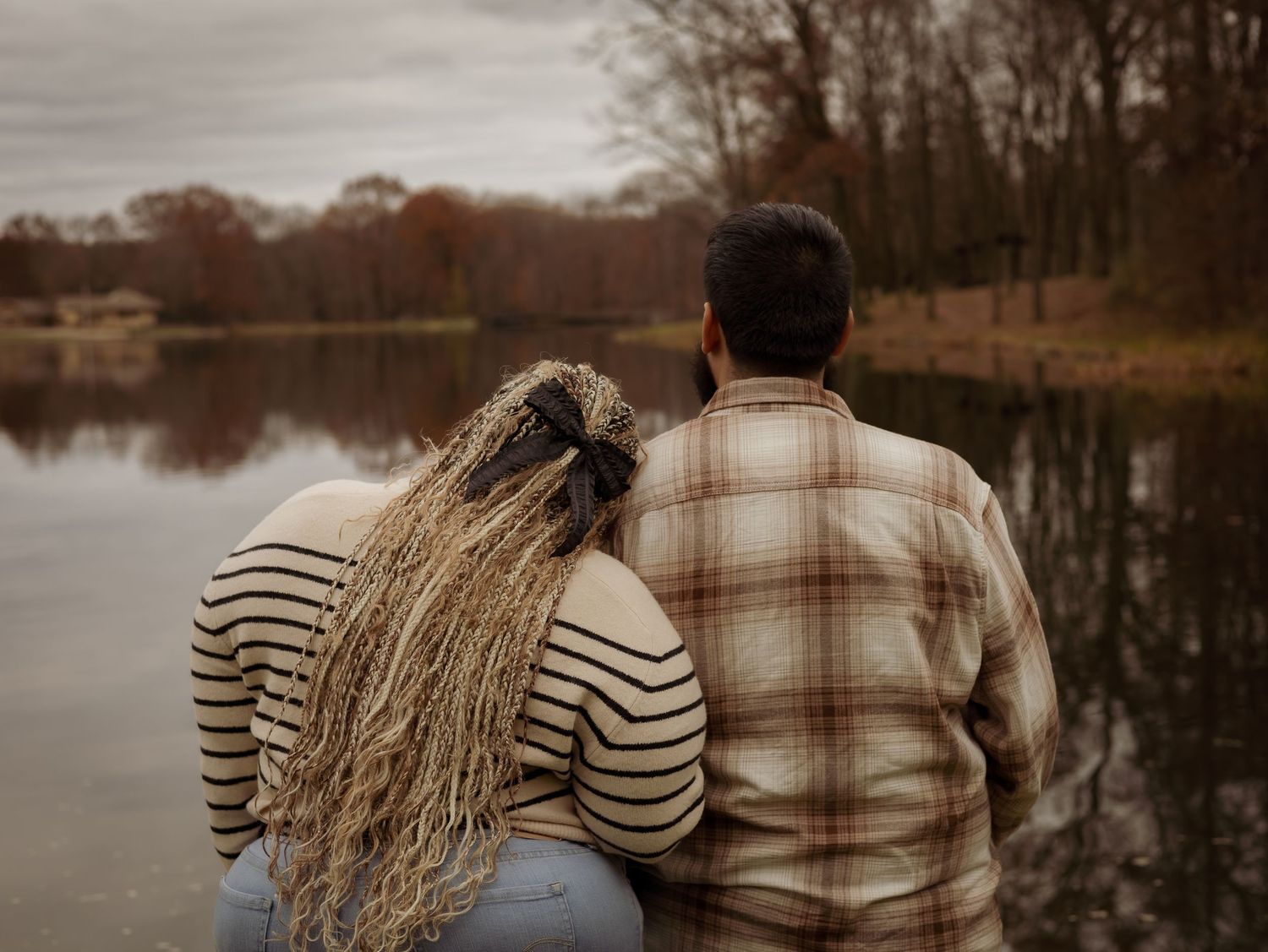 A couple sits together on a dock overlooking a tranquil lake on an autumn day.
