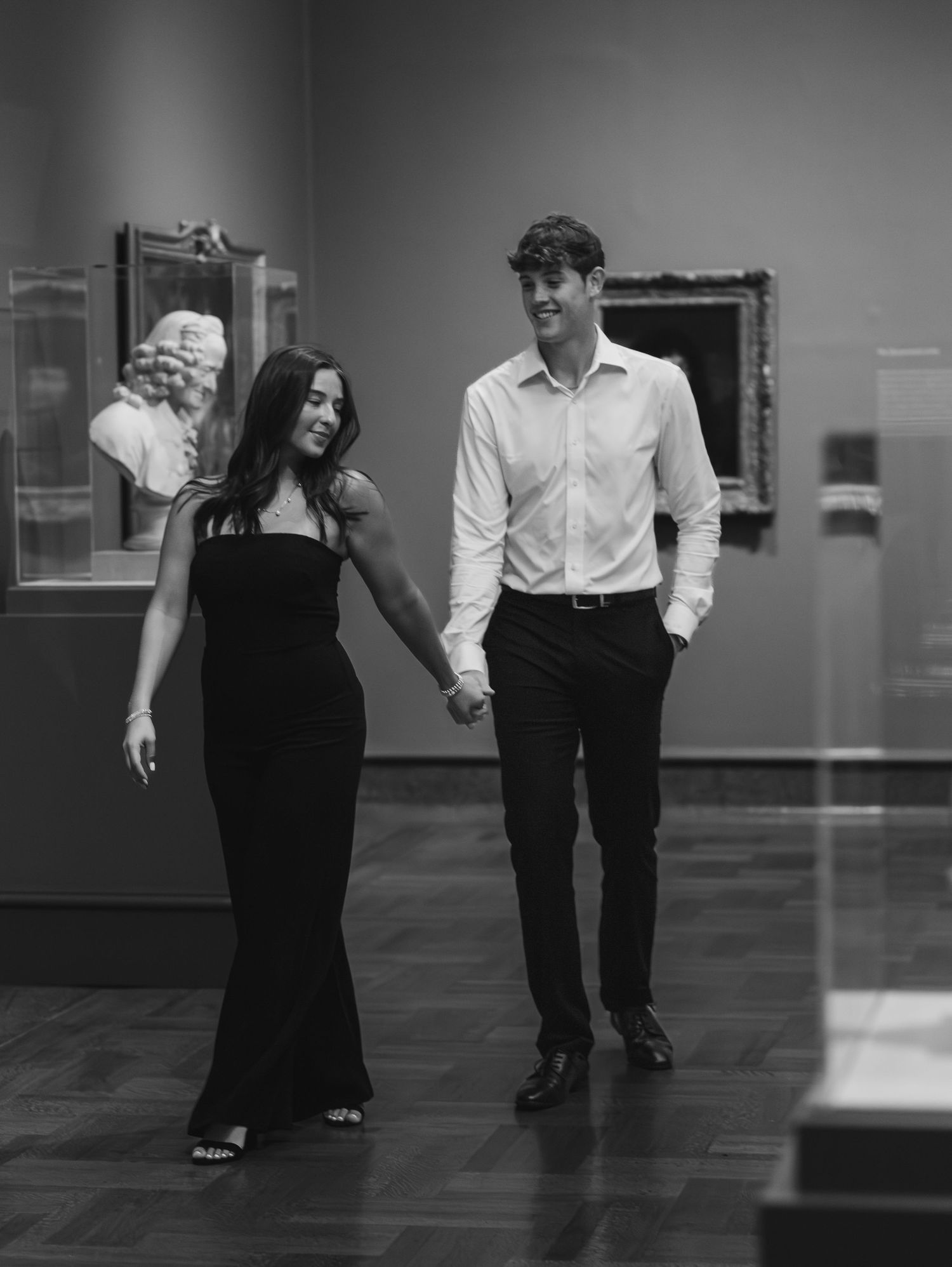 A couple in formal attire dances in a dimly lit gallery space.