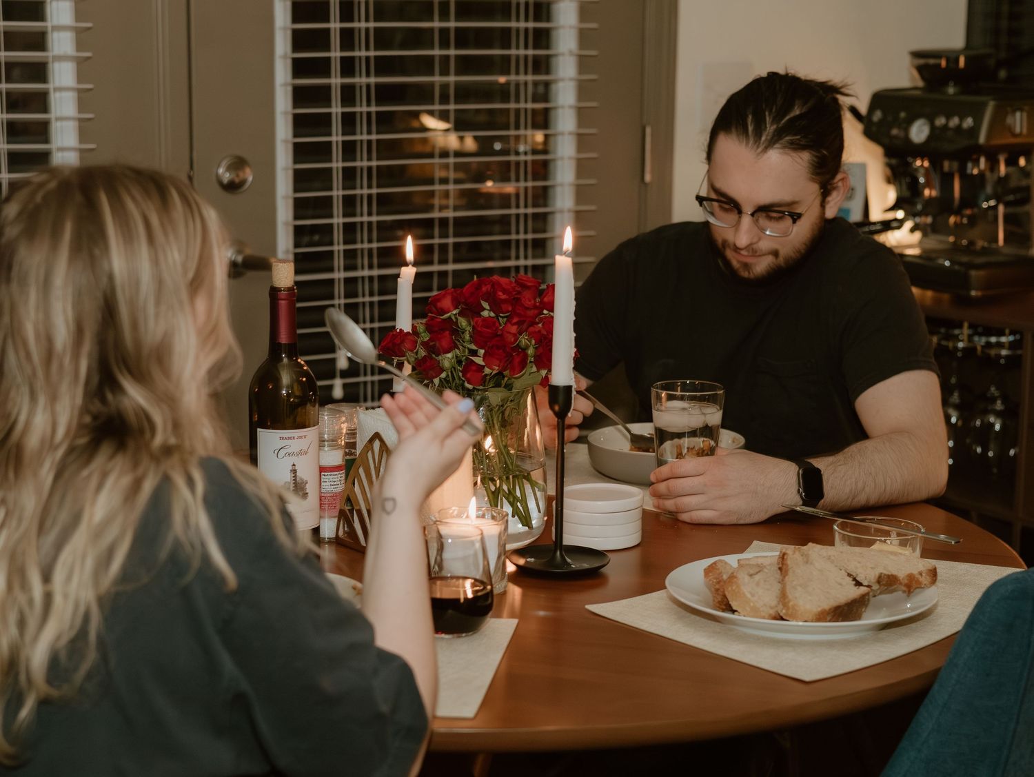 Two people share a meal at a dining table with candles and plates visible in warm indoor lighting.