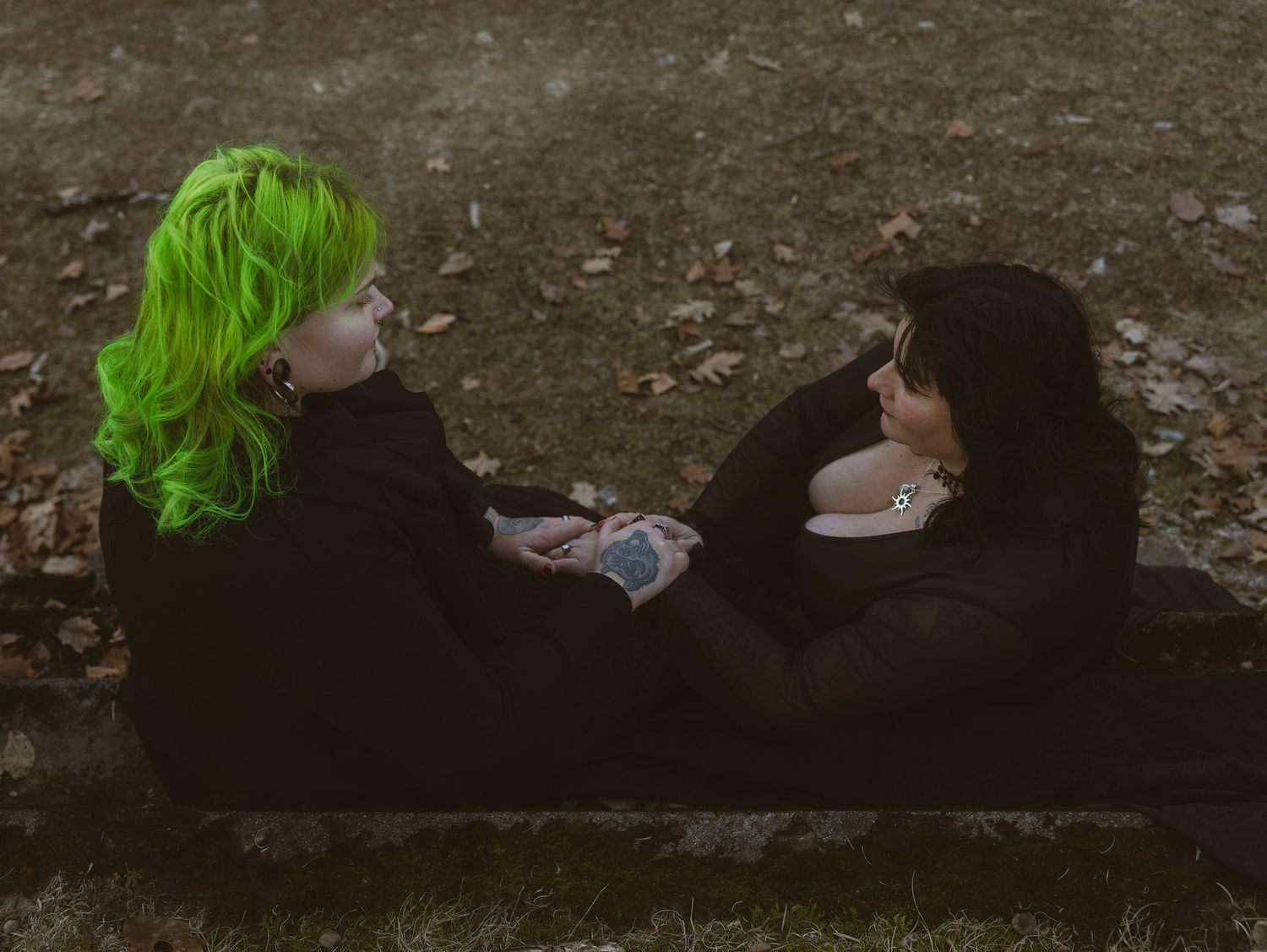 Person with bright green hair lying on dark ground in moody outdoor setting.