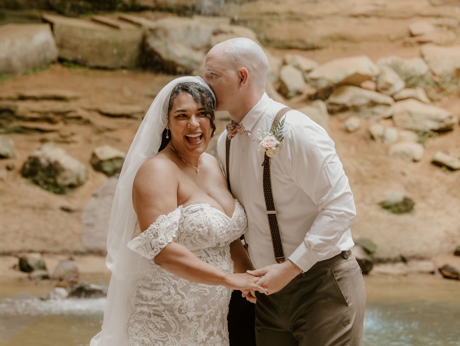 Joyful wedding couple sharing a romantic moment by a waterfall.