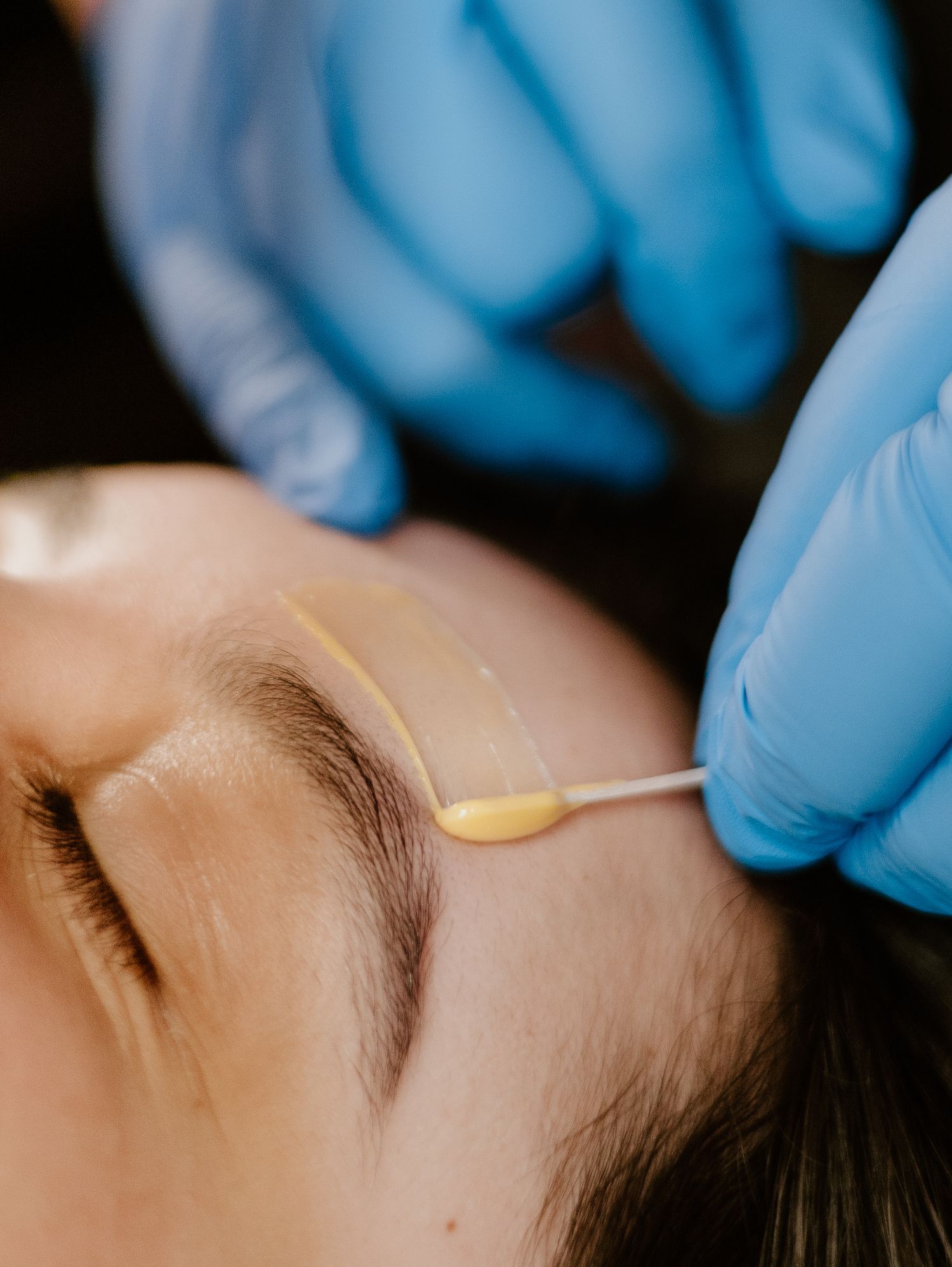 Close-up view of an aesthetician applying wax in preparation for eyebrow threading treatment.