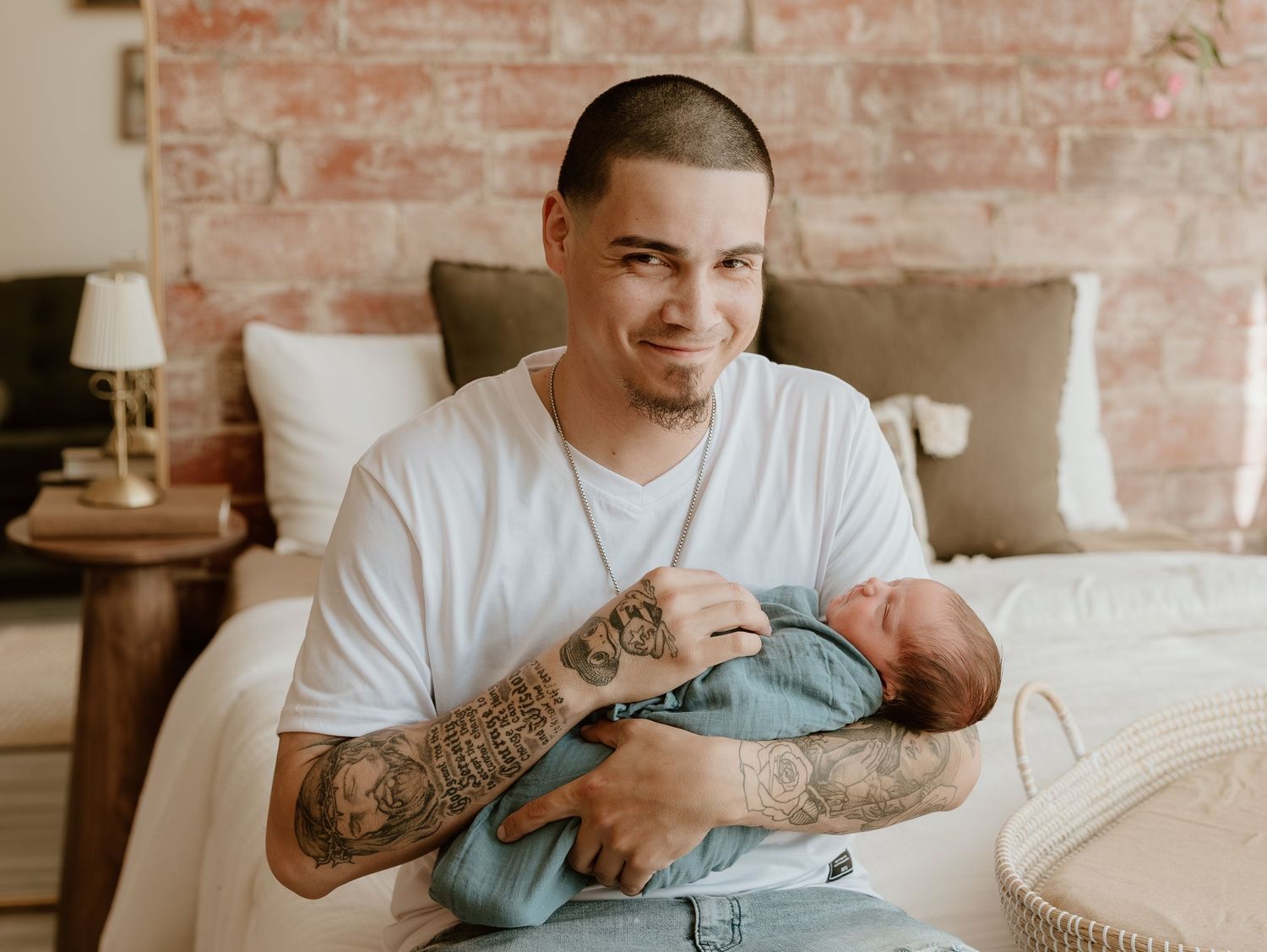Person with tattoos sitting on couch using mobile phone in modern room with exposed brick walls.