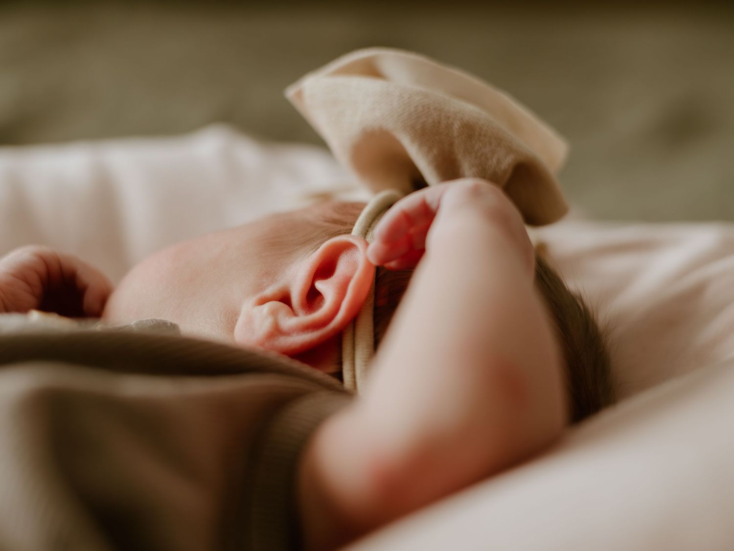 A person lies peacefully on soft beige bedding while resting in natural lighting.
