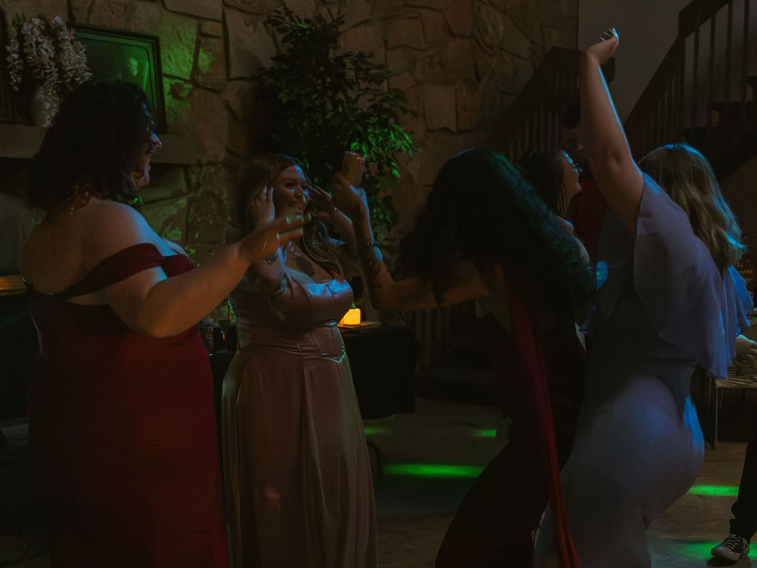 Women in formal gowns dancing at an elegant indoor party with green and amber mood lighting.