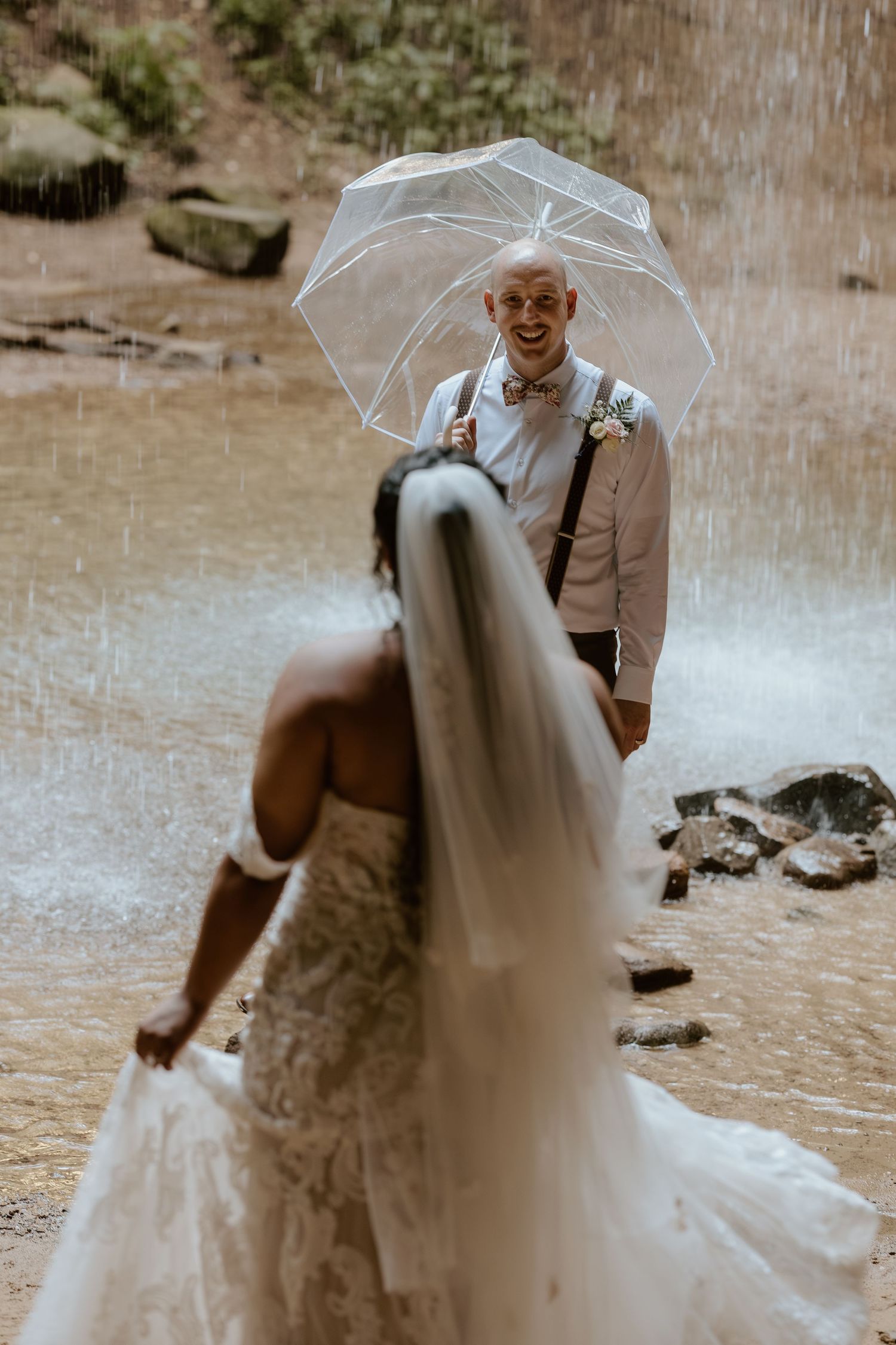 Romantic wedding moment captured under a clear umbrella in the rain.