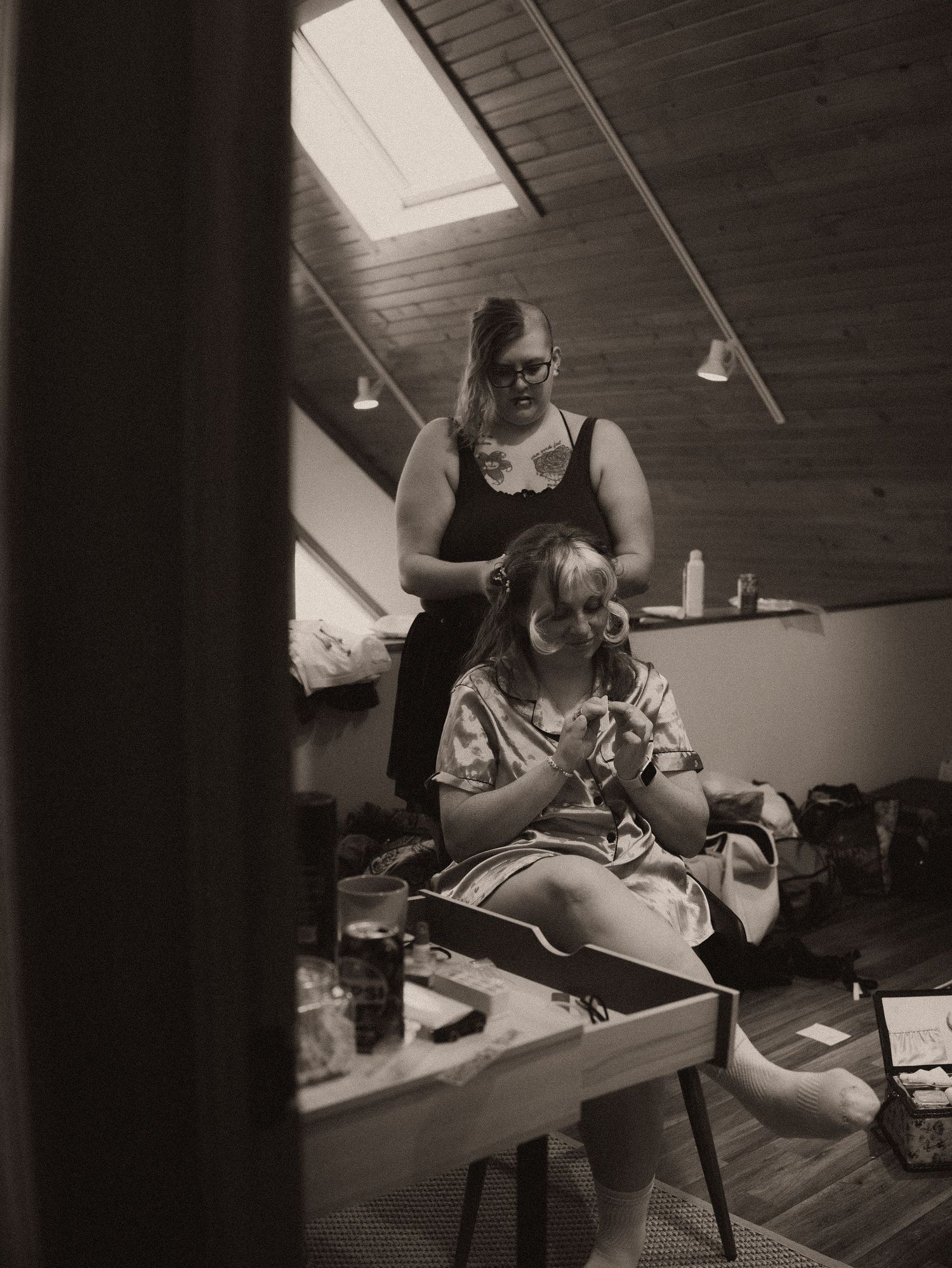 Black and white photo of wedding preparation with hair and makeup being styled in a rustic room.