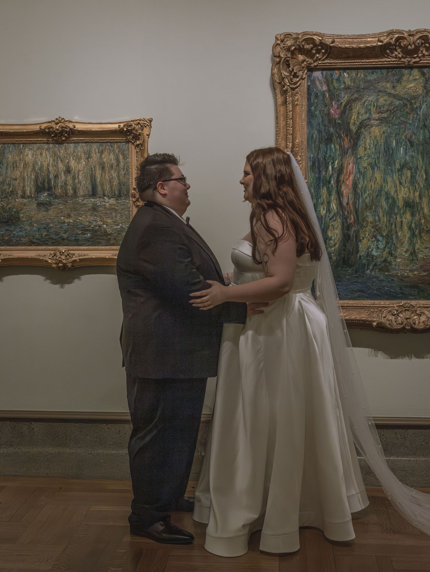 Couple in formal attire sharing an intimate moment in an art gallery with ornate framed paintings.