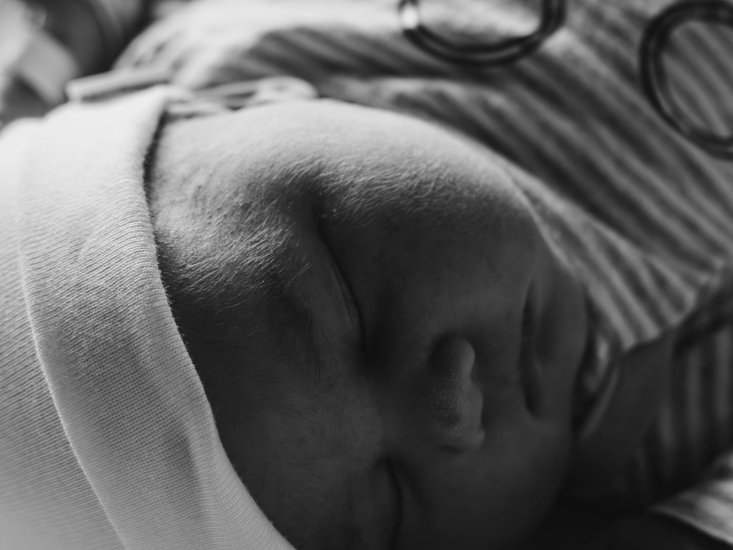 Black and white close-up photograph of a sleeping newborn baby wrapped in a white blanket.