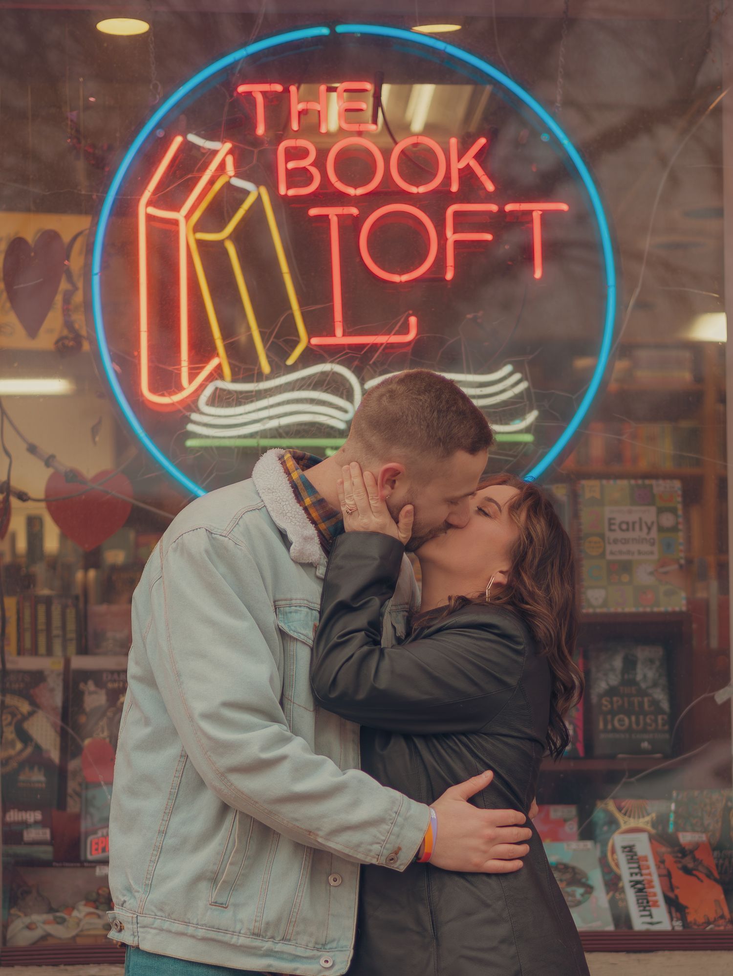 Couple sharing intimate moment in front of illuminated neon bookstore sign display.