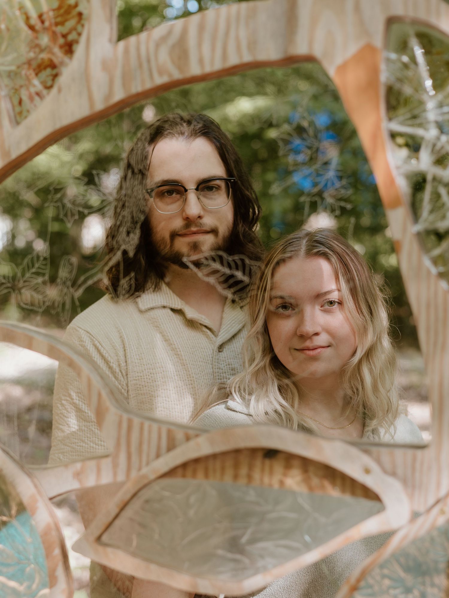 A couple poses together in an artistic framed shot with natural forest backdrop.