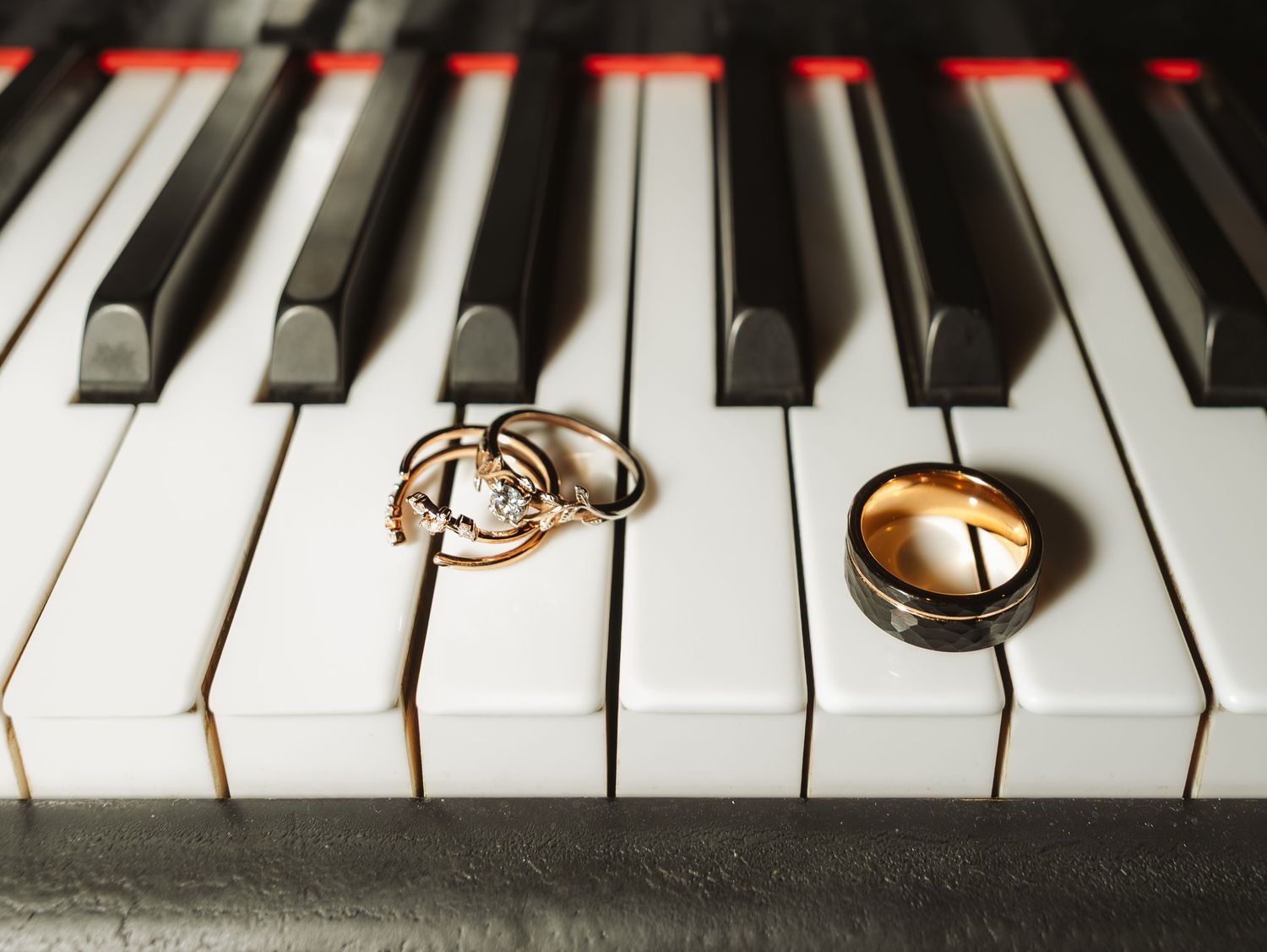 Two gold wedding rings and a diamond engagement ring resting on black and white piano keys.