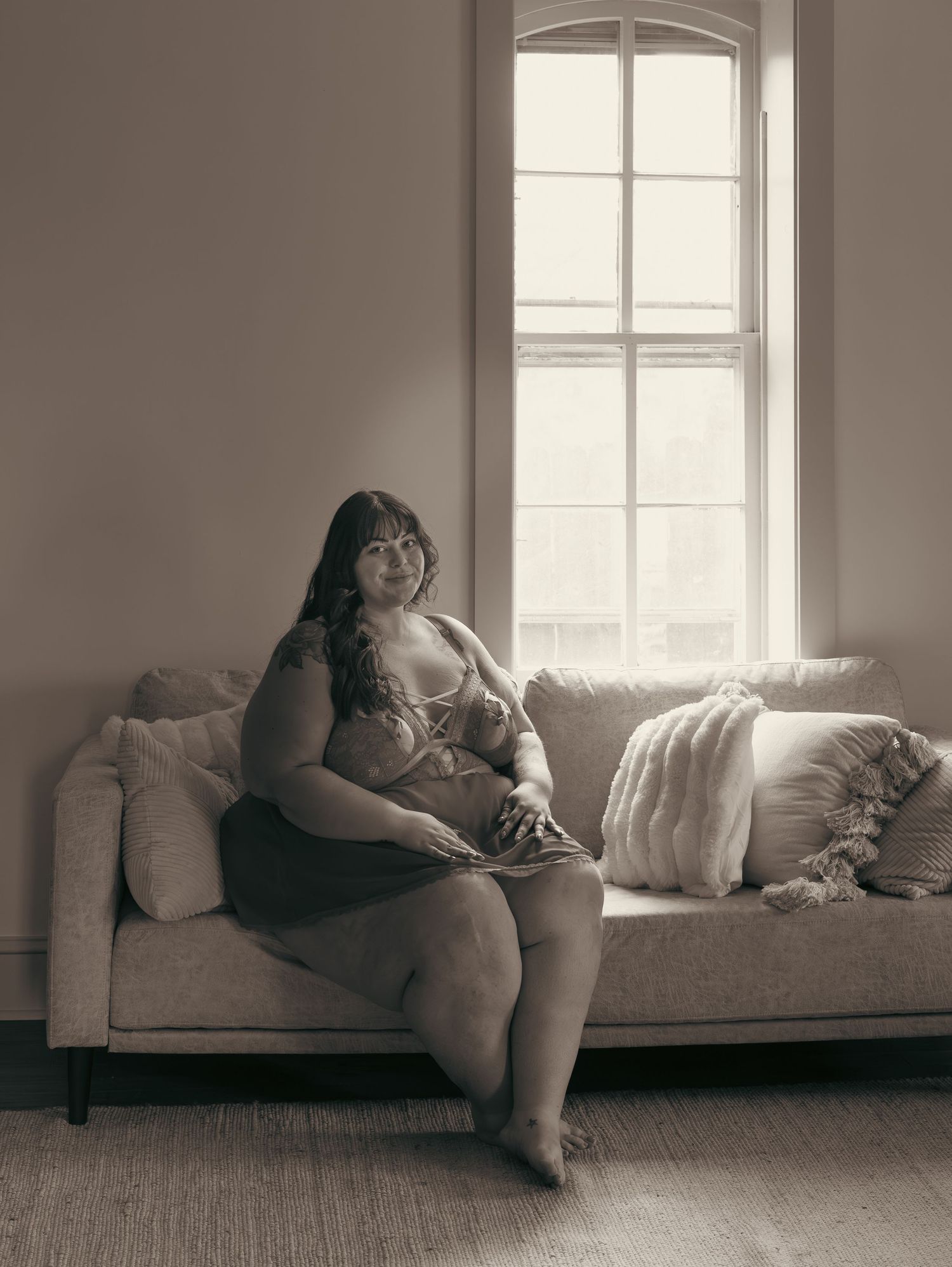 Sepia-toned portrait by a bright window in a minimalist room setting.