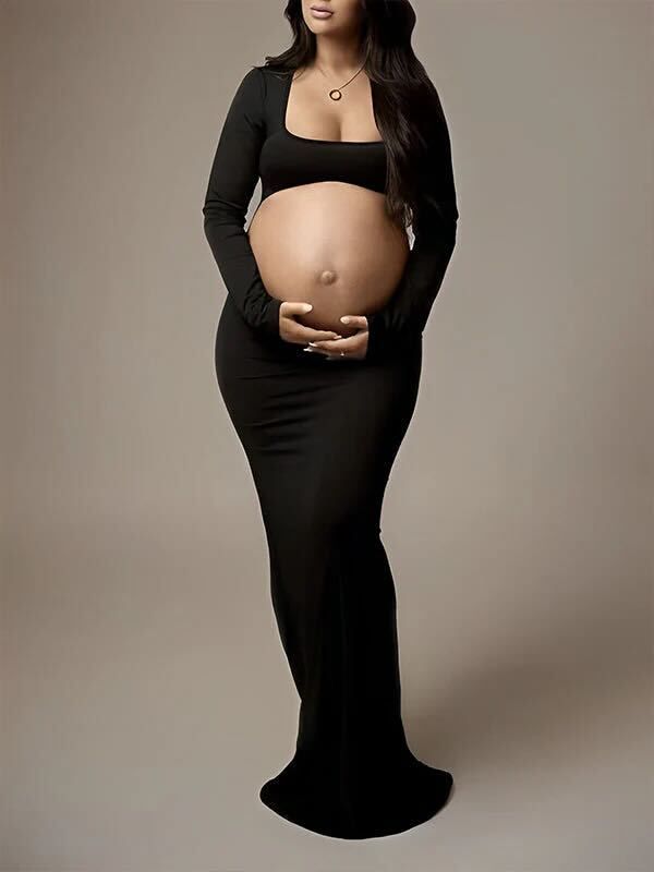 A pregnant figure in a fitted black maxi dress with long sleeves stands elegantly against a neutral background.