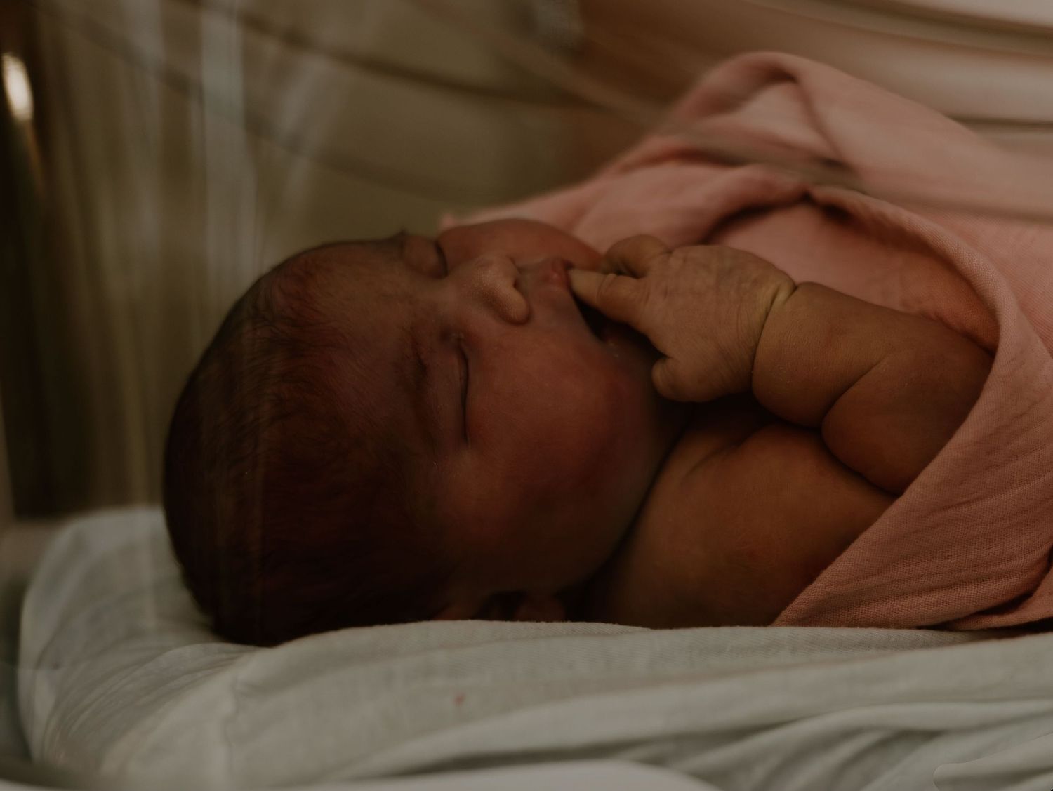 Newborn baby sleeping peacefully wrapped in pink blanket.