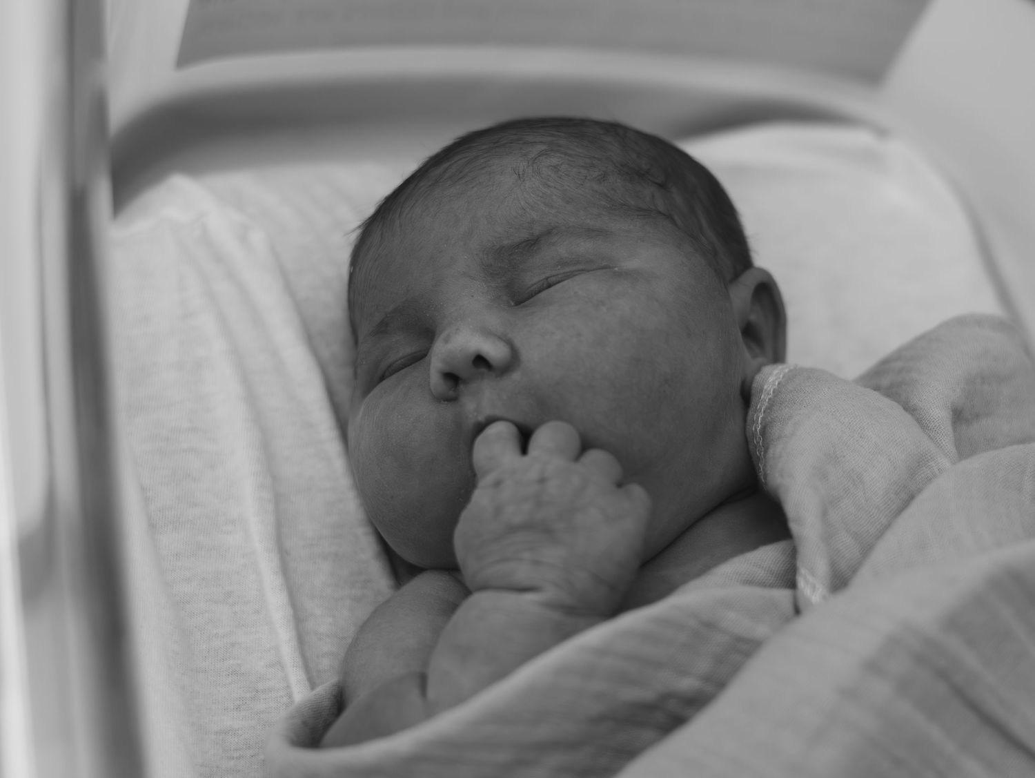 Newborn babies sleeping peacefully in hospital bassinets lined up in a row.