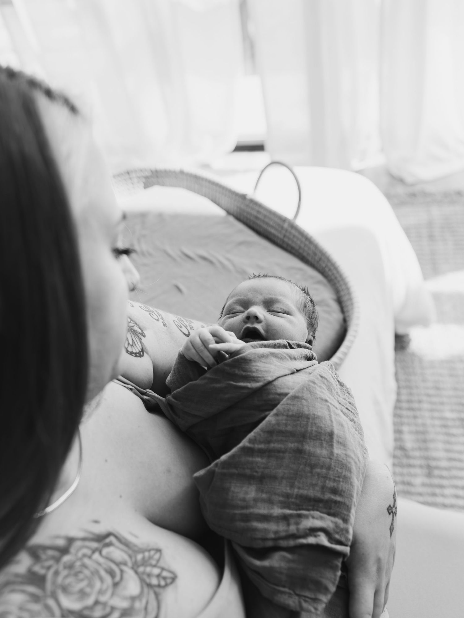 A peaceful newborn baby rests on white bedding while wearing a sage colored outfit.