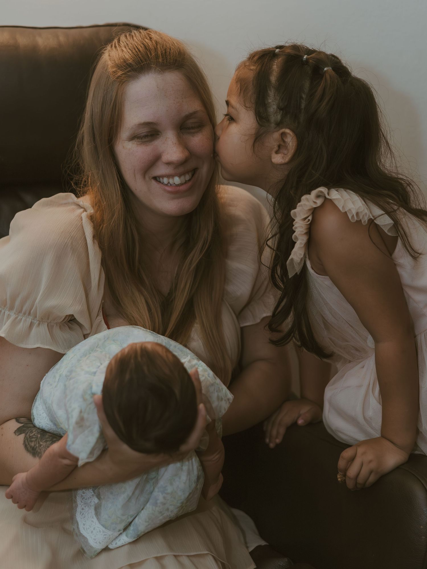 Sweet family moment captured on a couch with gentle kisses and embraces in soft, warm lighting.