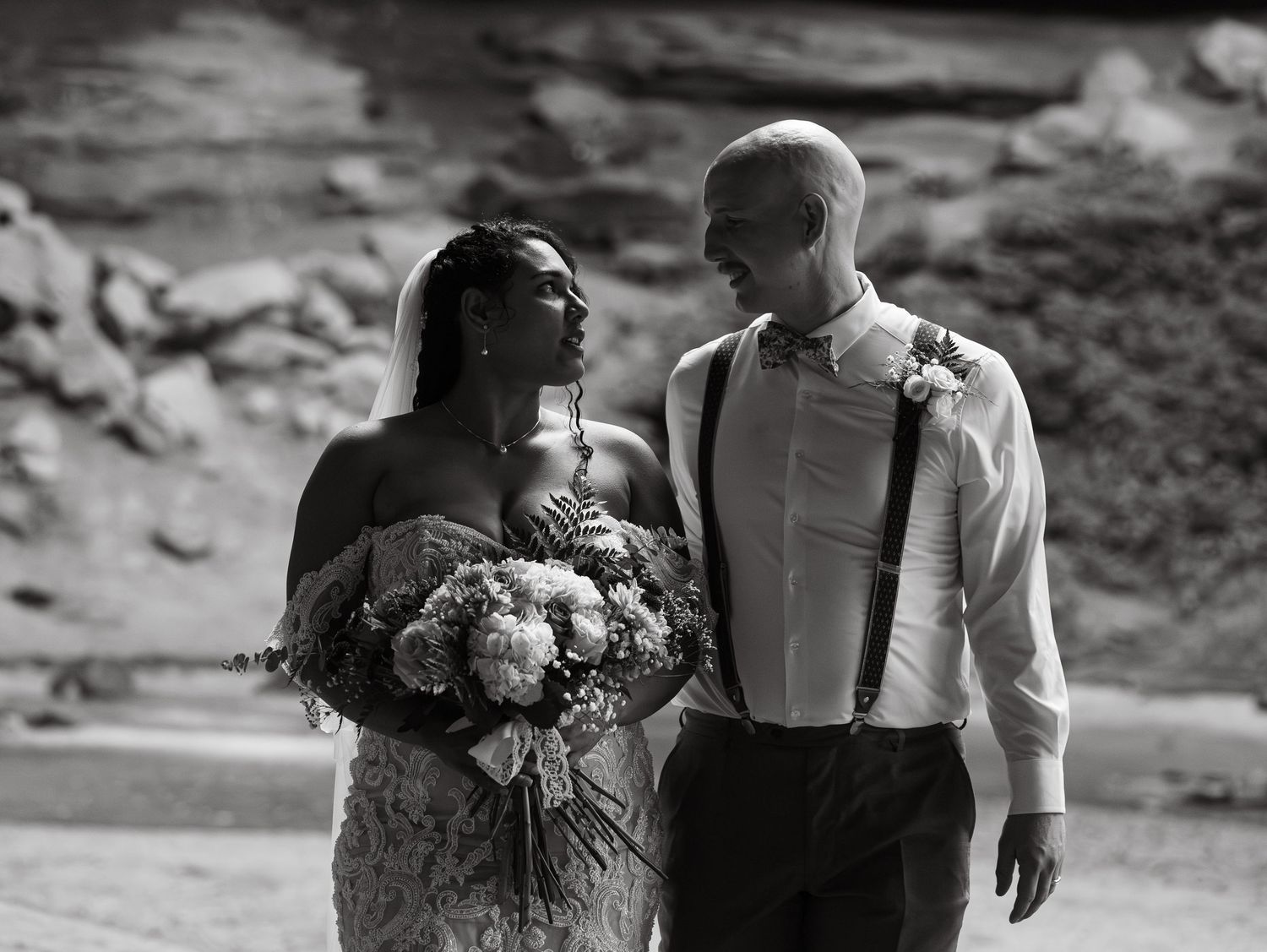 Black and white wedding portrait with couple walking through natural scenery.