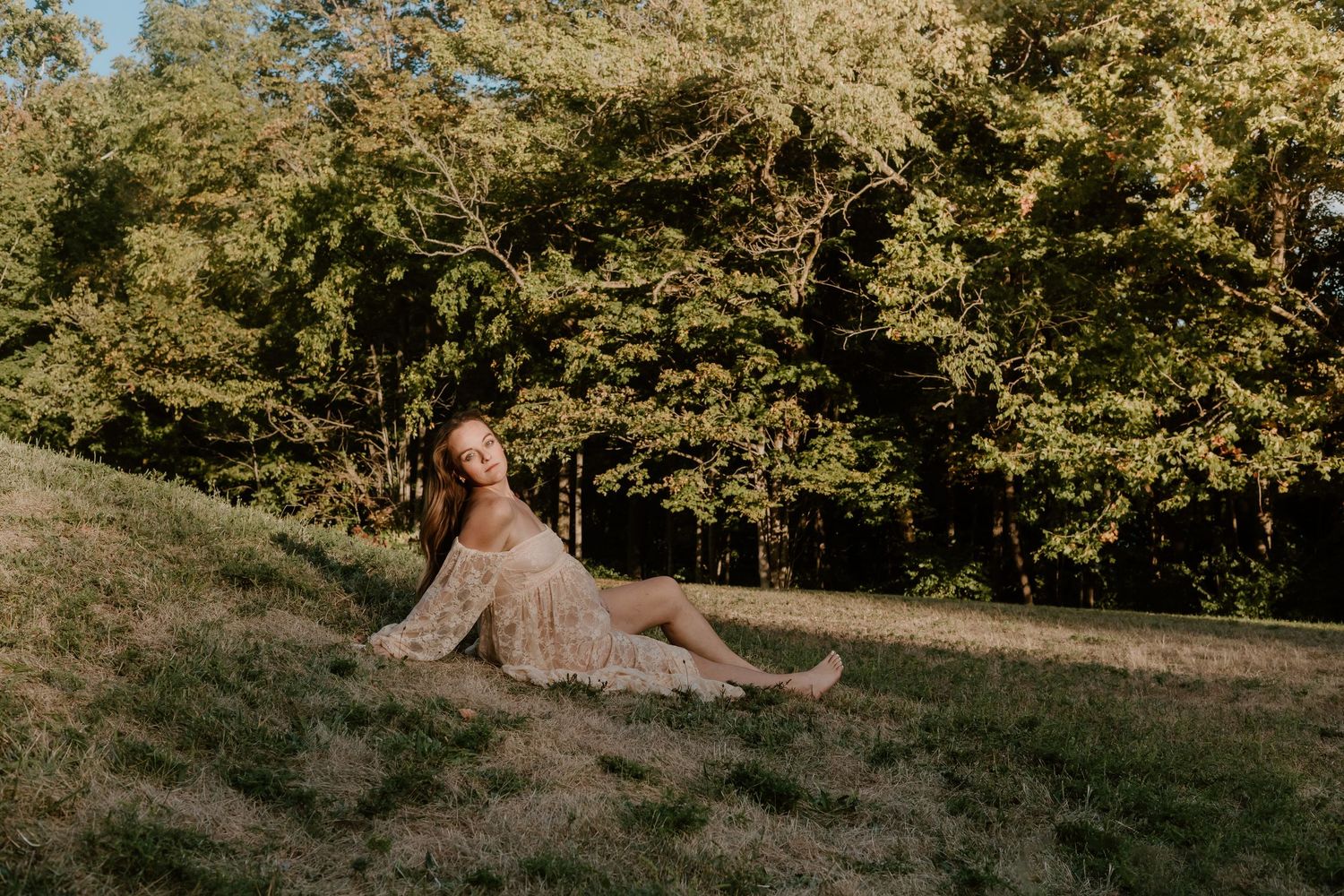 A couple poses together in a sunlit meadow surrounded by autumn trees during a golden hour photoshoot.