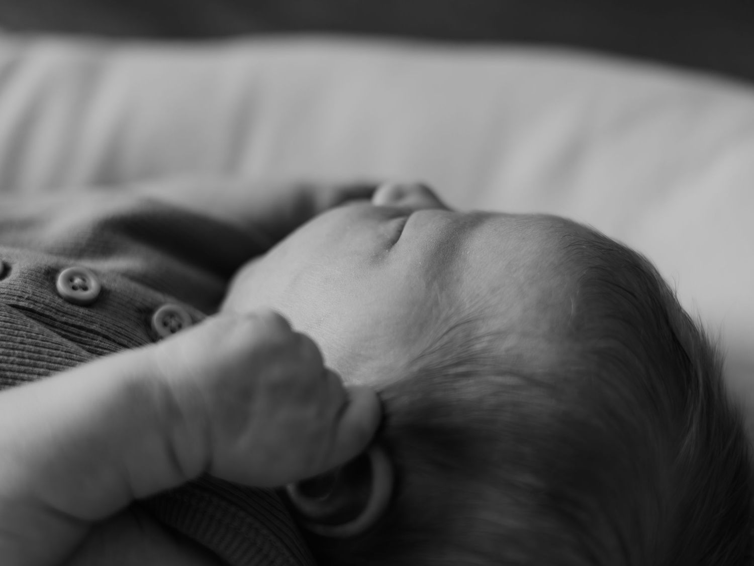 Close-up of a sleeping baby's tiny hand resting on soft white bedding in natural light.