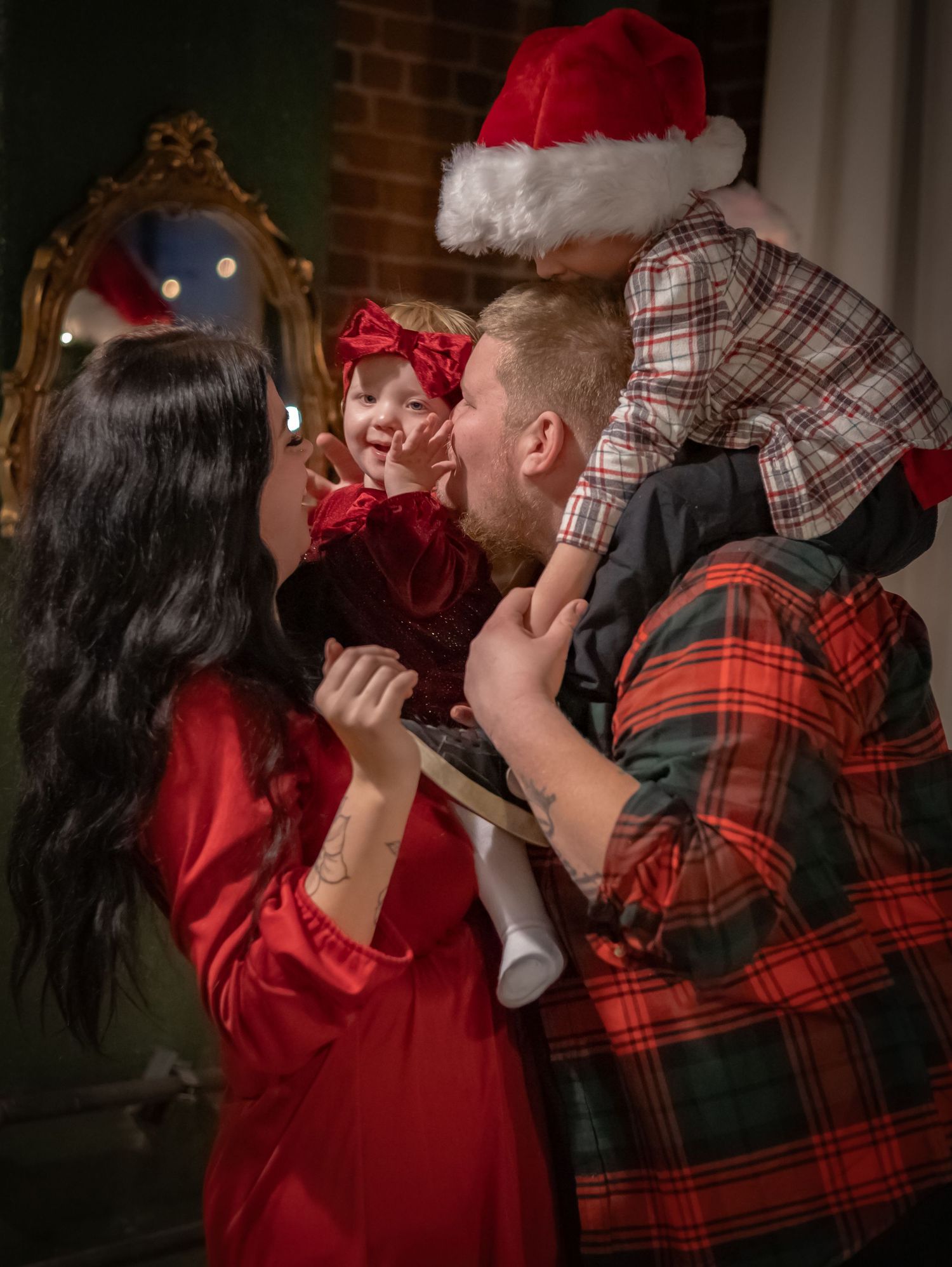 Family in red and plaid holiday outfits sharing intimate moment by decorated Christmas tree.
