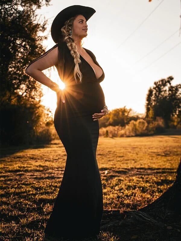 Silhouetted figure in black dress and cowboy hat poses in a field during golden hour sunset.
