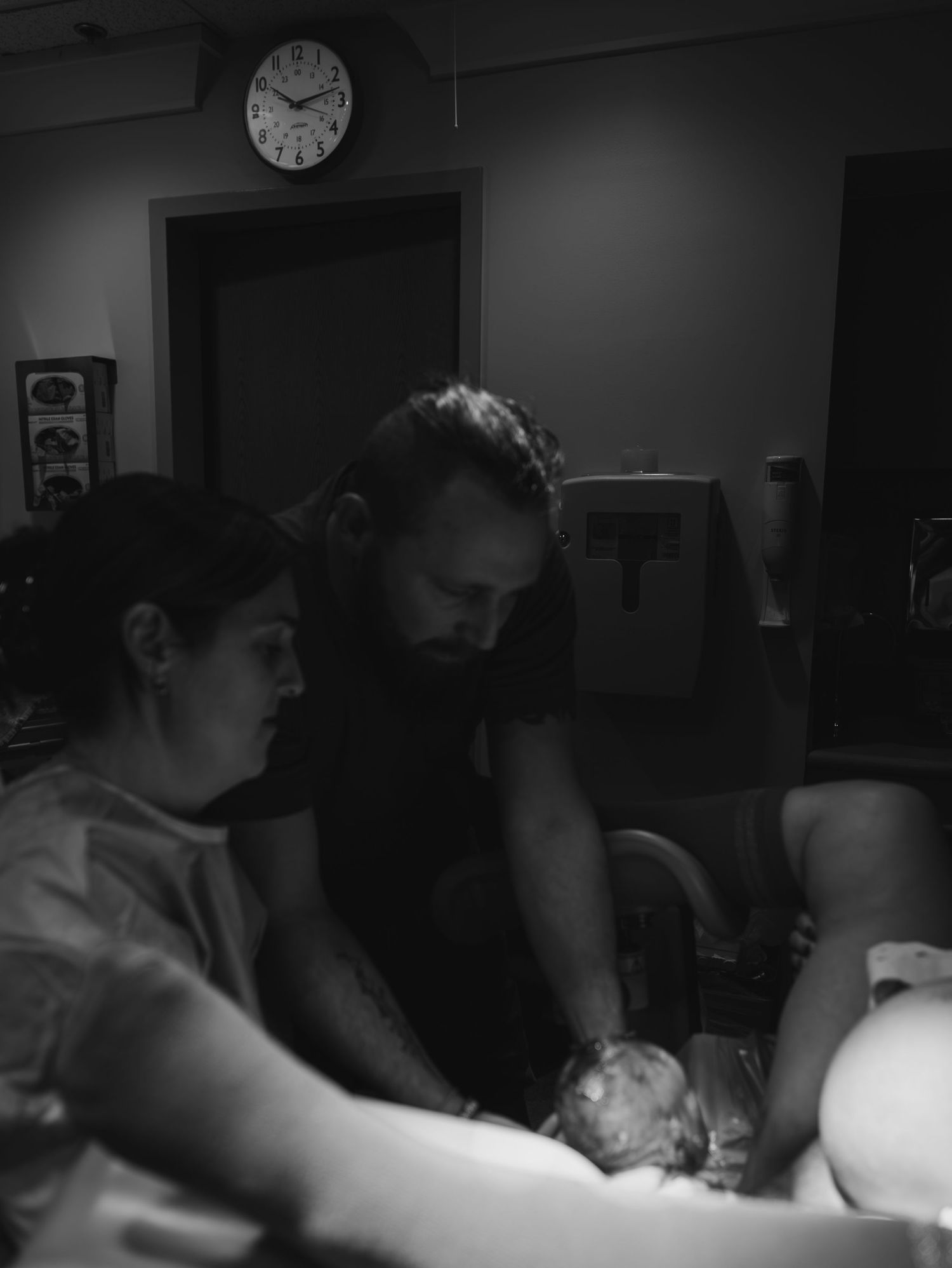A black and white photograph shows medical staff in a dimly lit room engaged in a medical procedure.