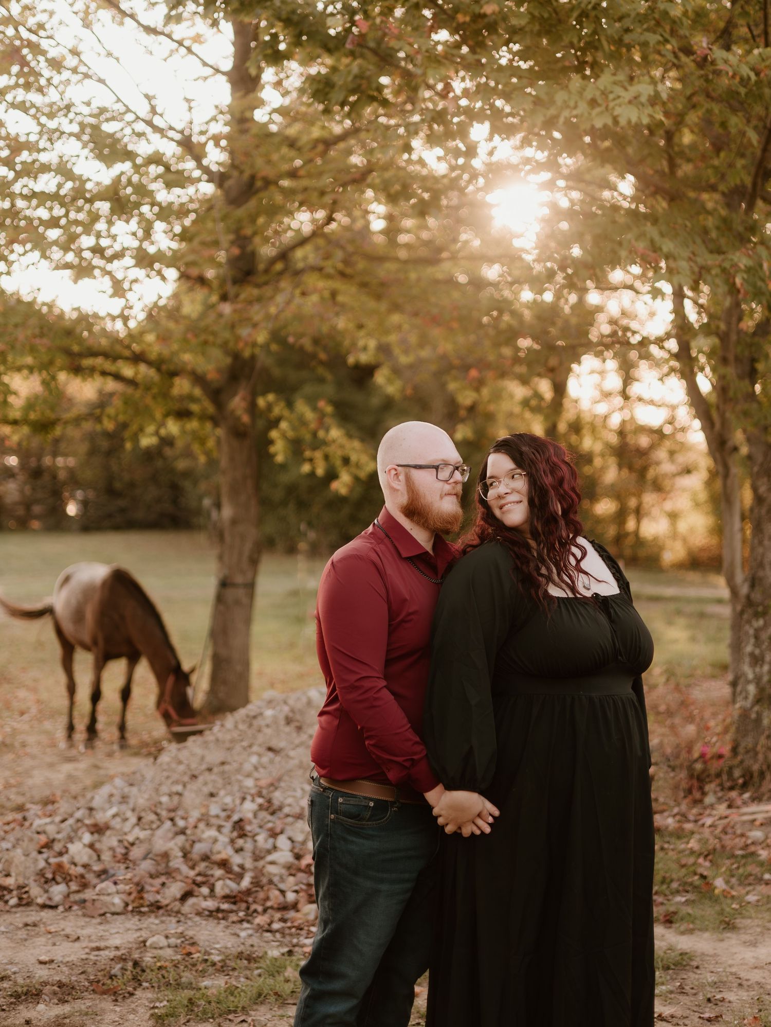 A couple shares a romantic moment in a fall setting with autumn leaves scattered on the ground at sunset.