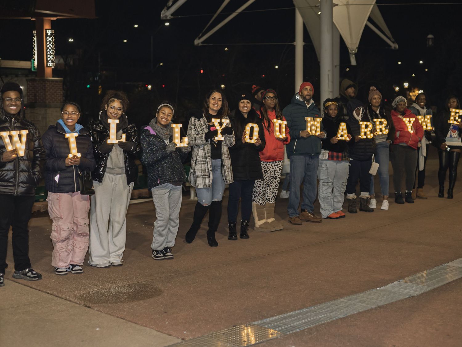 Students hold illuminated letters spelling 'WILL U MARRY' during a nighttime marriage proposal event.
