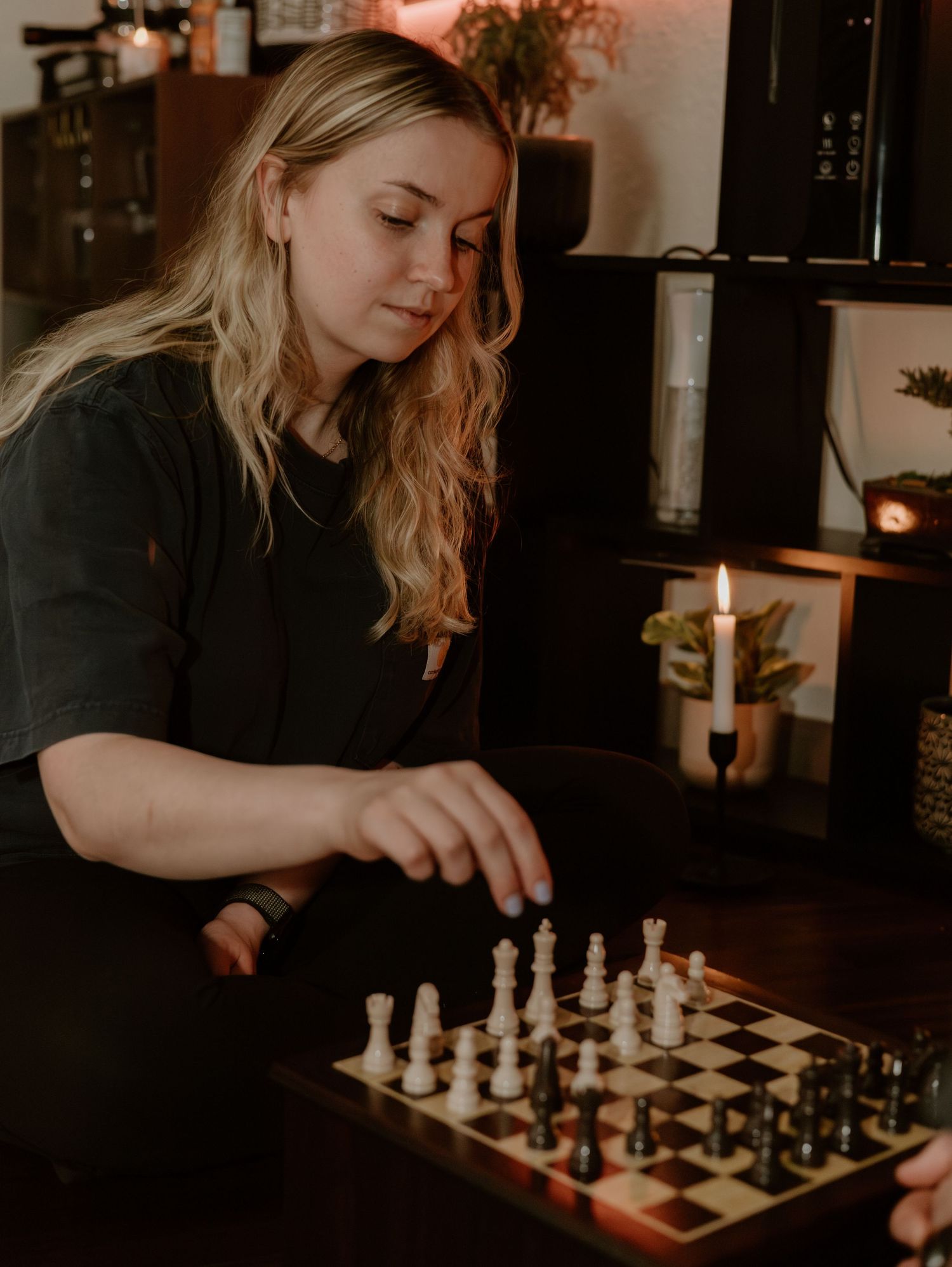 A person playing chess in a dimly lit room with candles creating a cozy and intimate atmosphere.
