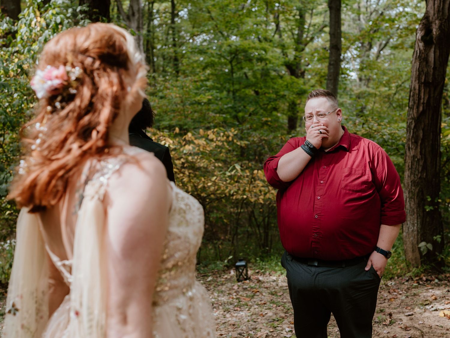 A couple shares an intimate moment in a wooded forest setting wearing wedding attire.