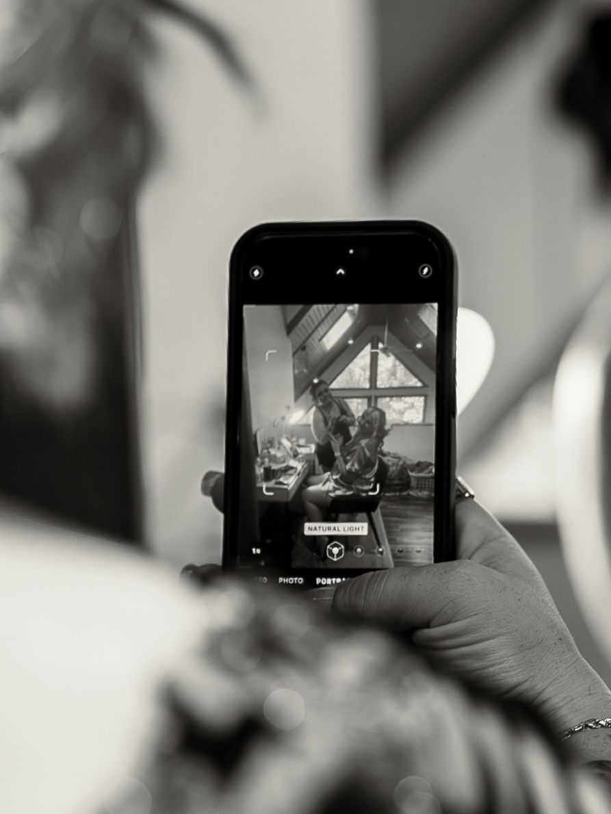 A hand holds a smartphone displaying a black and white photo being taken through its camera viewfinder.