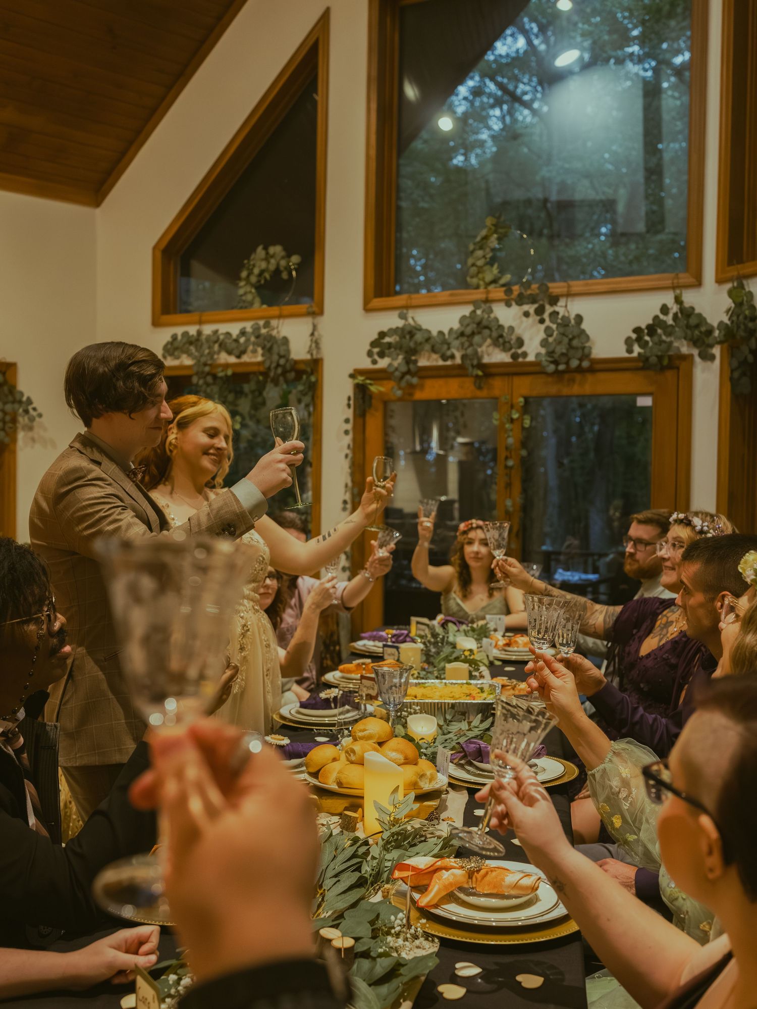 Wedding guests raise their glasses in a toast during a cozy indoor reception.
