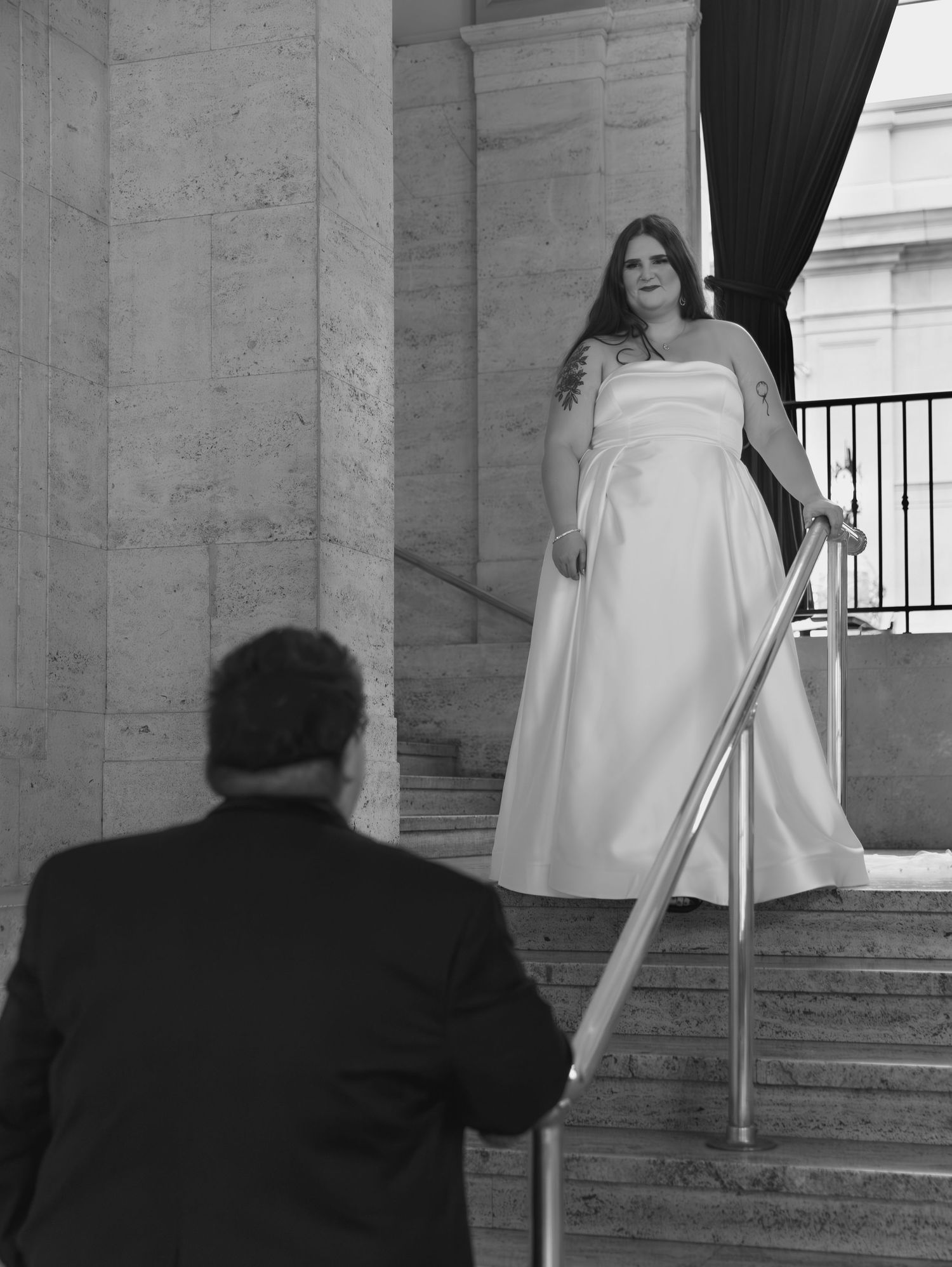Bride in white dress photographed from behind on marble steps.