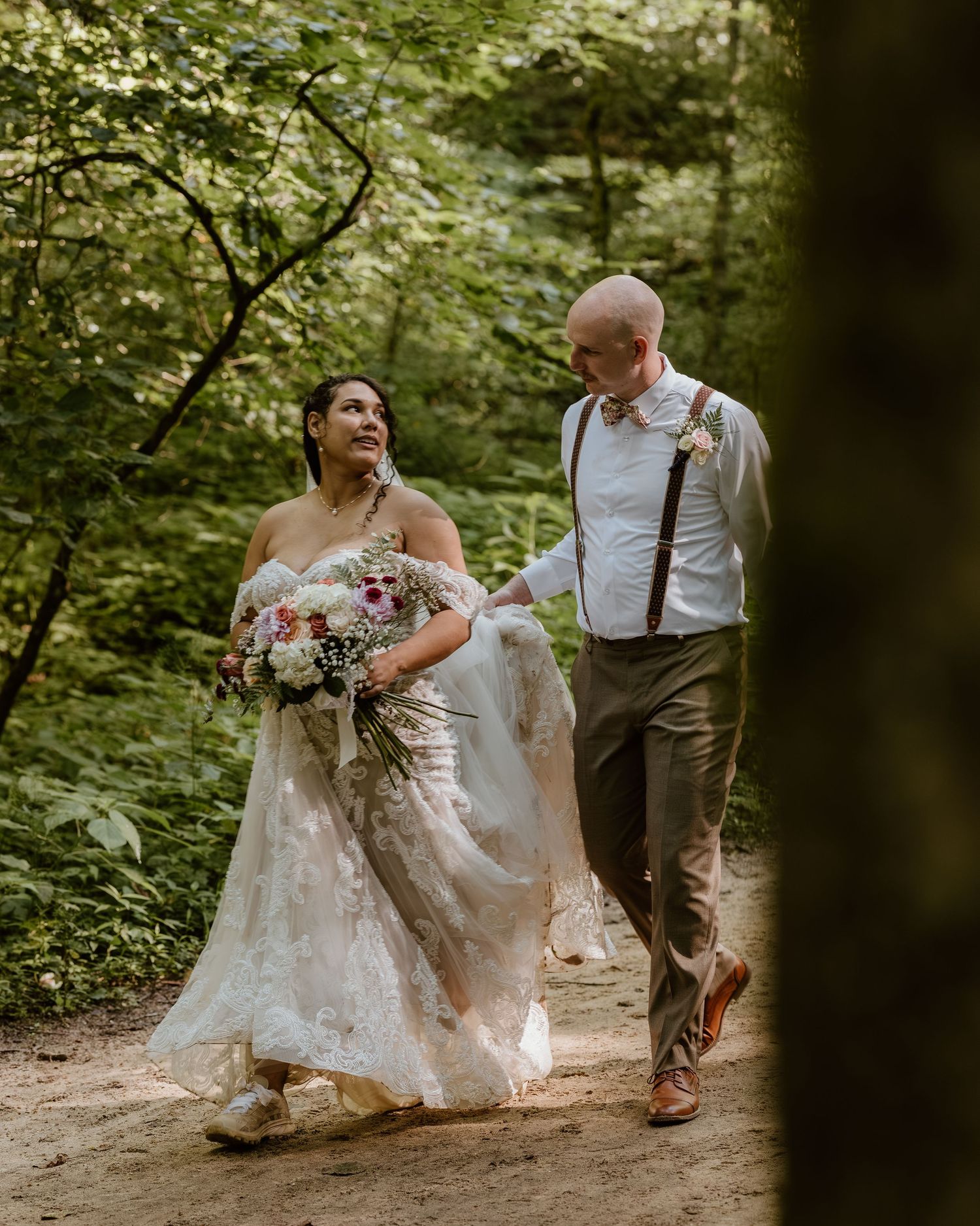 Couple walking through a lush forest path during their wedding photoshoot.