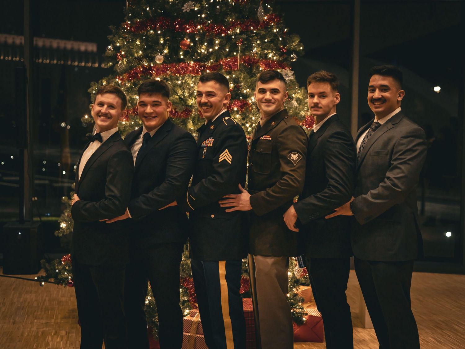 Friends in military and formal attire gathered around a beautifully lit Christmas tree.