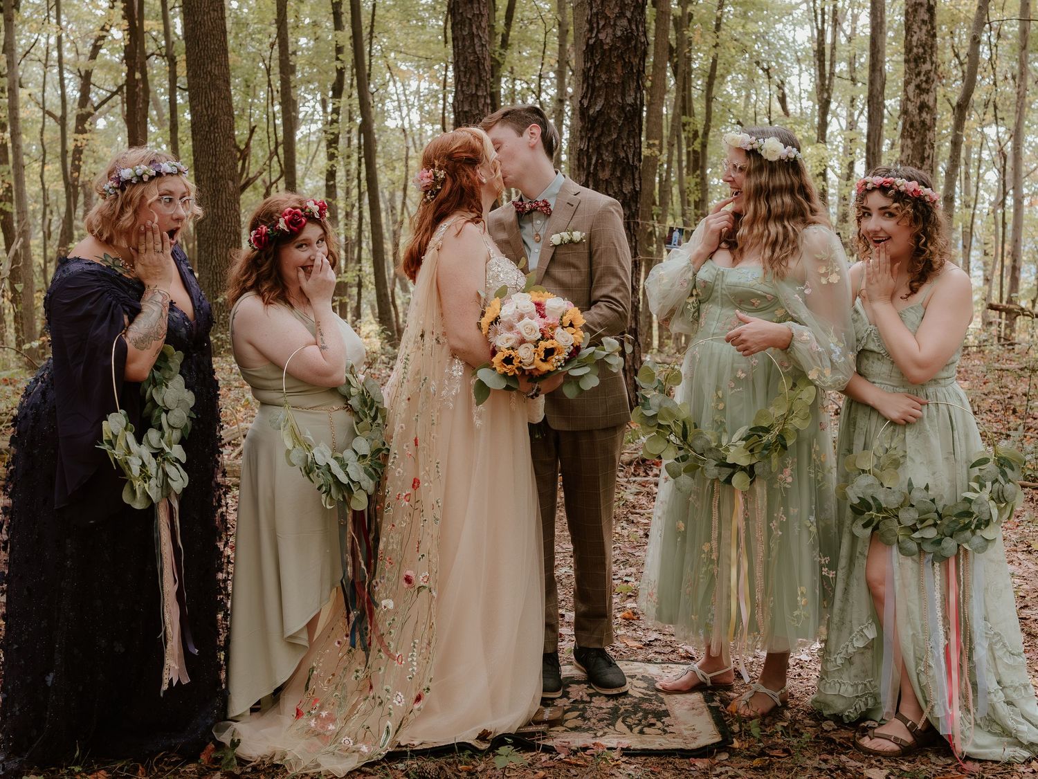 Wedding party in sage green and cream dresses poses together in a sunlit forest setting.