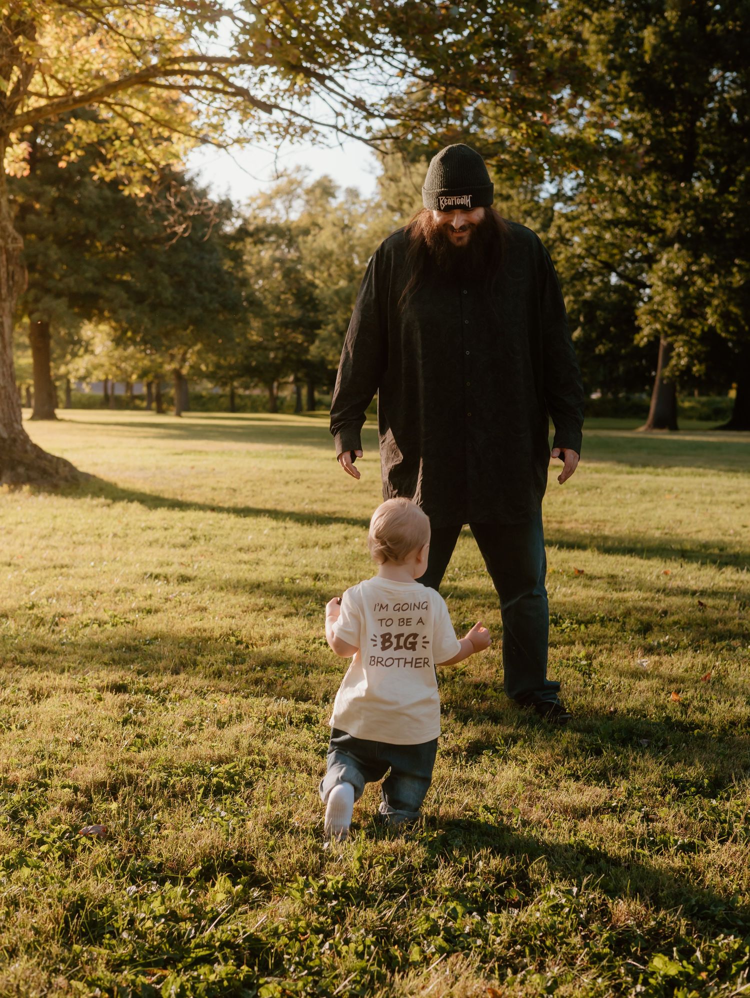 A small child and adult walk together through a sunlit autumn park during golden hour.