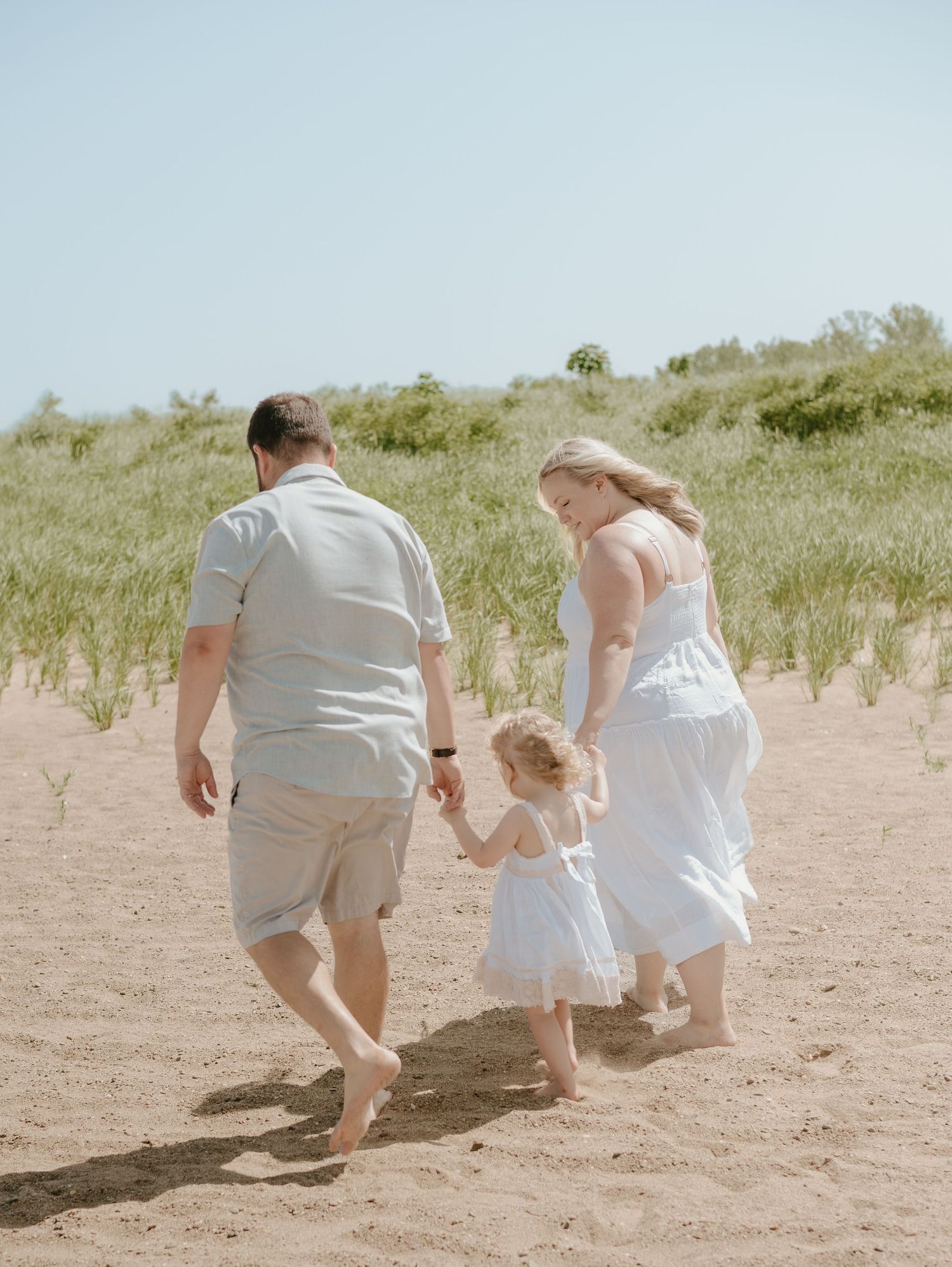 Family walking up sandy dunes together on a bright summer day at the beach.