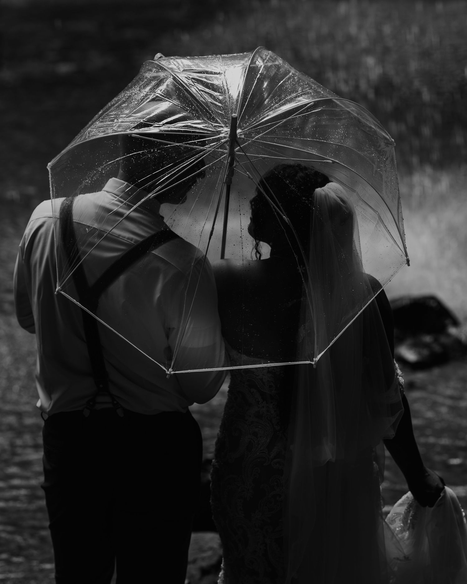 Black and white photo of a bride and groom sharing a clear umbrella in the rain on their wedding day.
