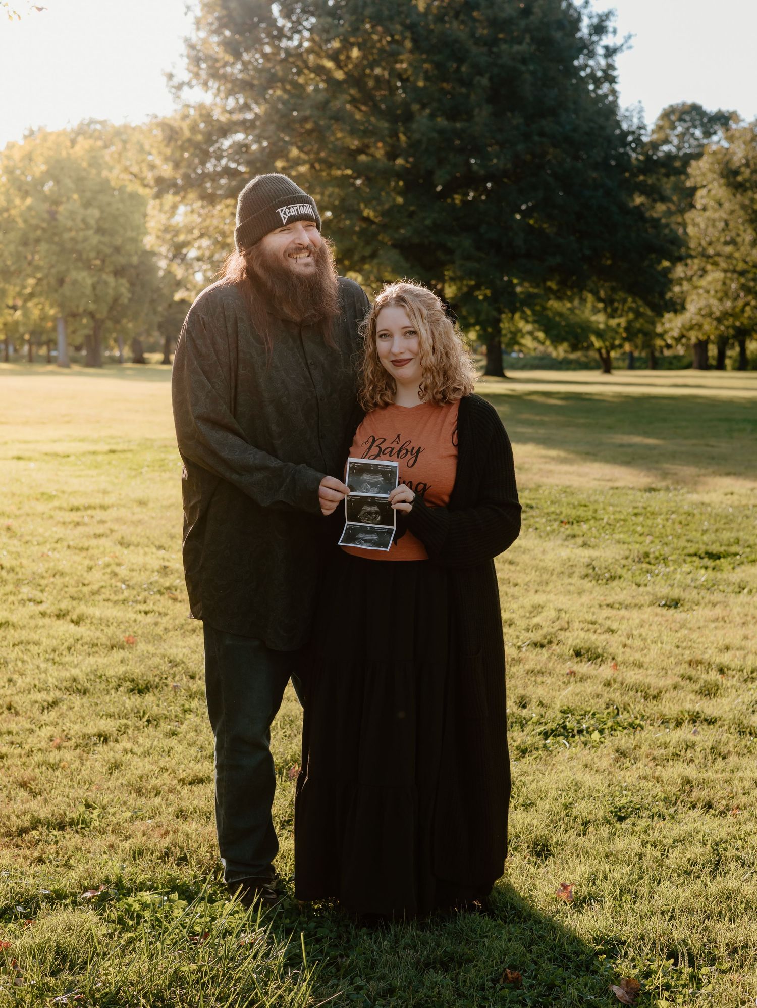 A couple sits together in a sunny field during golden hour sharing a joyful moment.